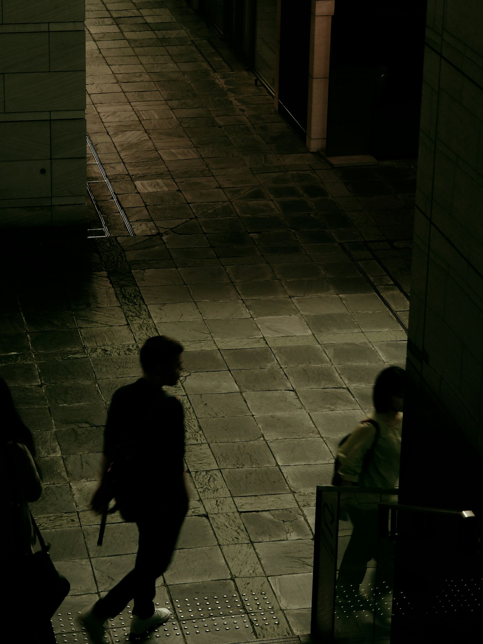 Siluetas de personas caminando sobre un pavimento de piedra tenuemente iluminado