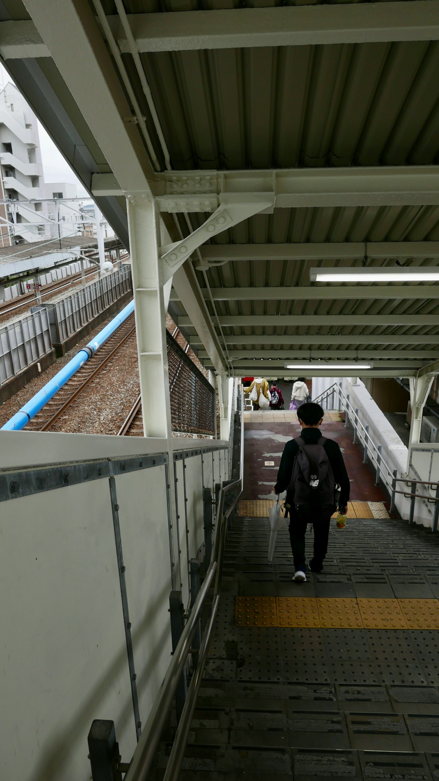 Orang yang berjalan menuruni tangga di stasiun kereta dengan rel terlihat