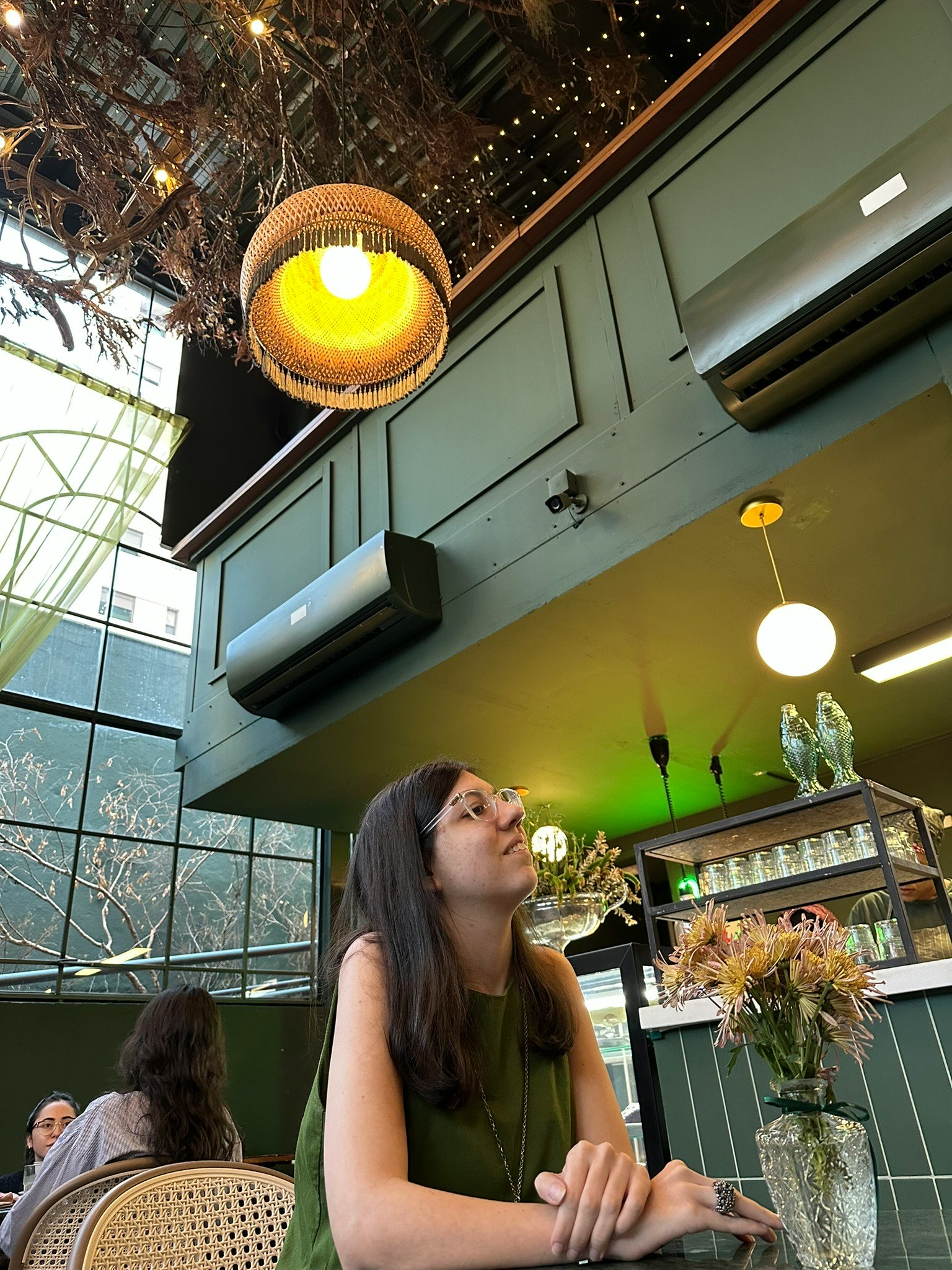 カフェ店内で花と照明を見上げる女性