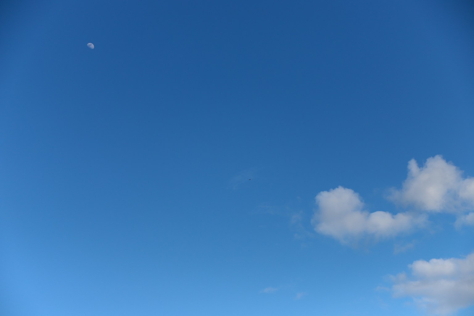 Langit biru dengan awan putih dan bulan kecil