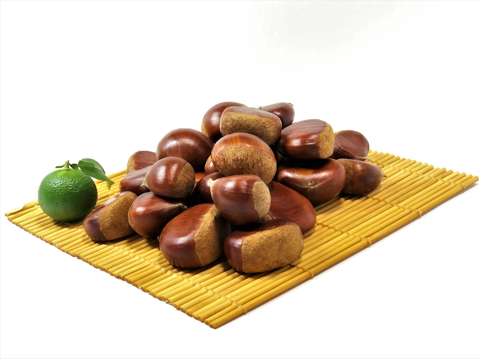 Ein Haufen brauner Kastanien mit einer grünen Zitrusfrucht auf einer Bambusmatte