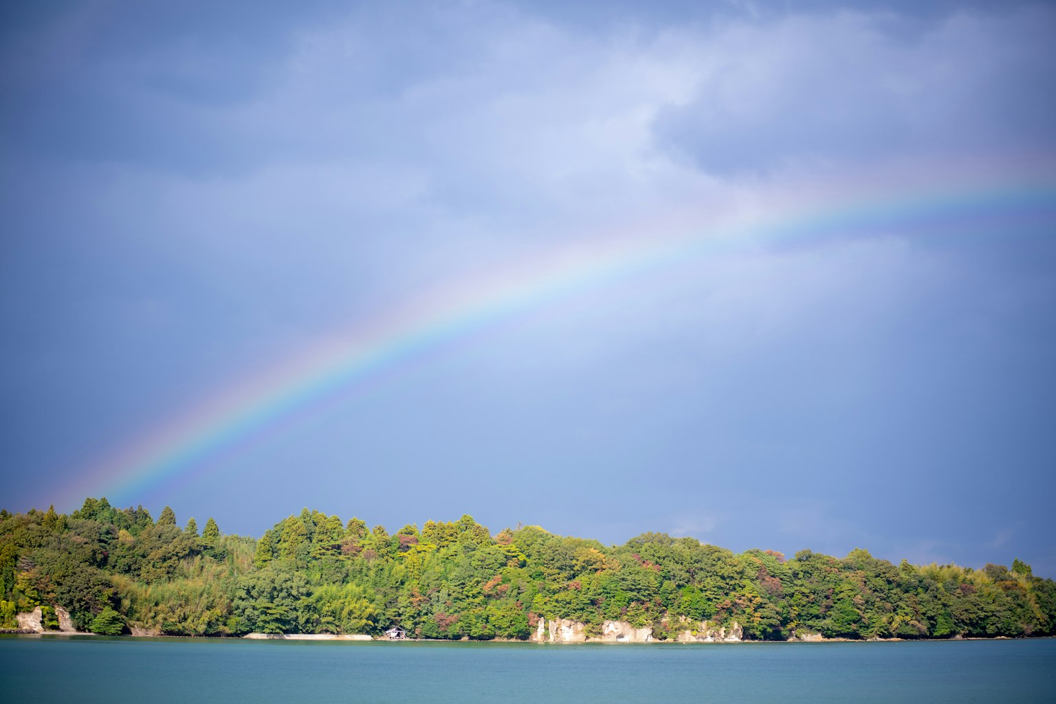 Un arcobaleno si estende sopra un'isola verde sotto un cielo blu