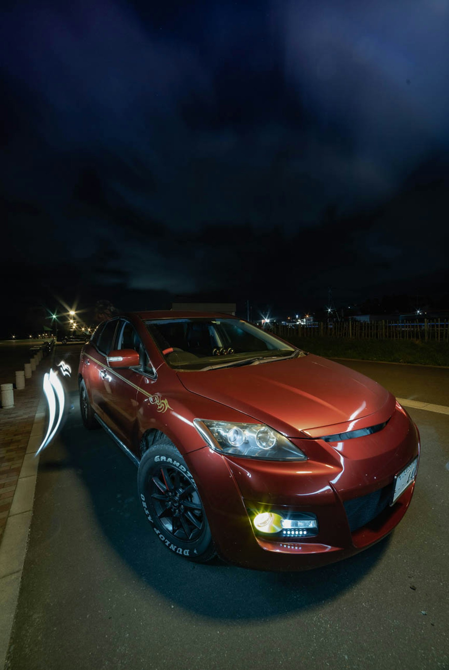Mobil merah diparkir di bawah langit malam menampilkan sisi dan depan