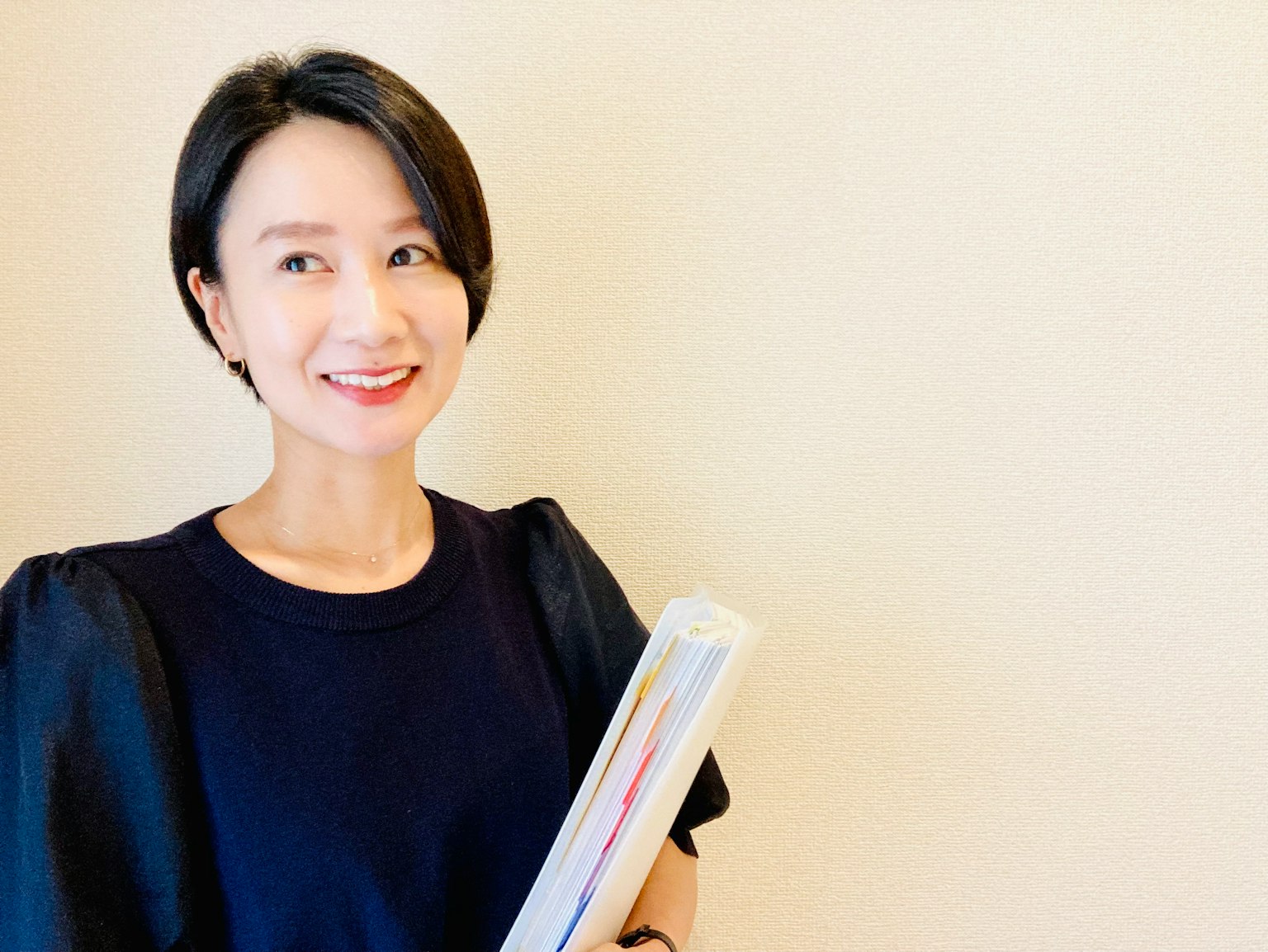 一位女性微笑著穿著黑色上衣，手裡拿著文件