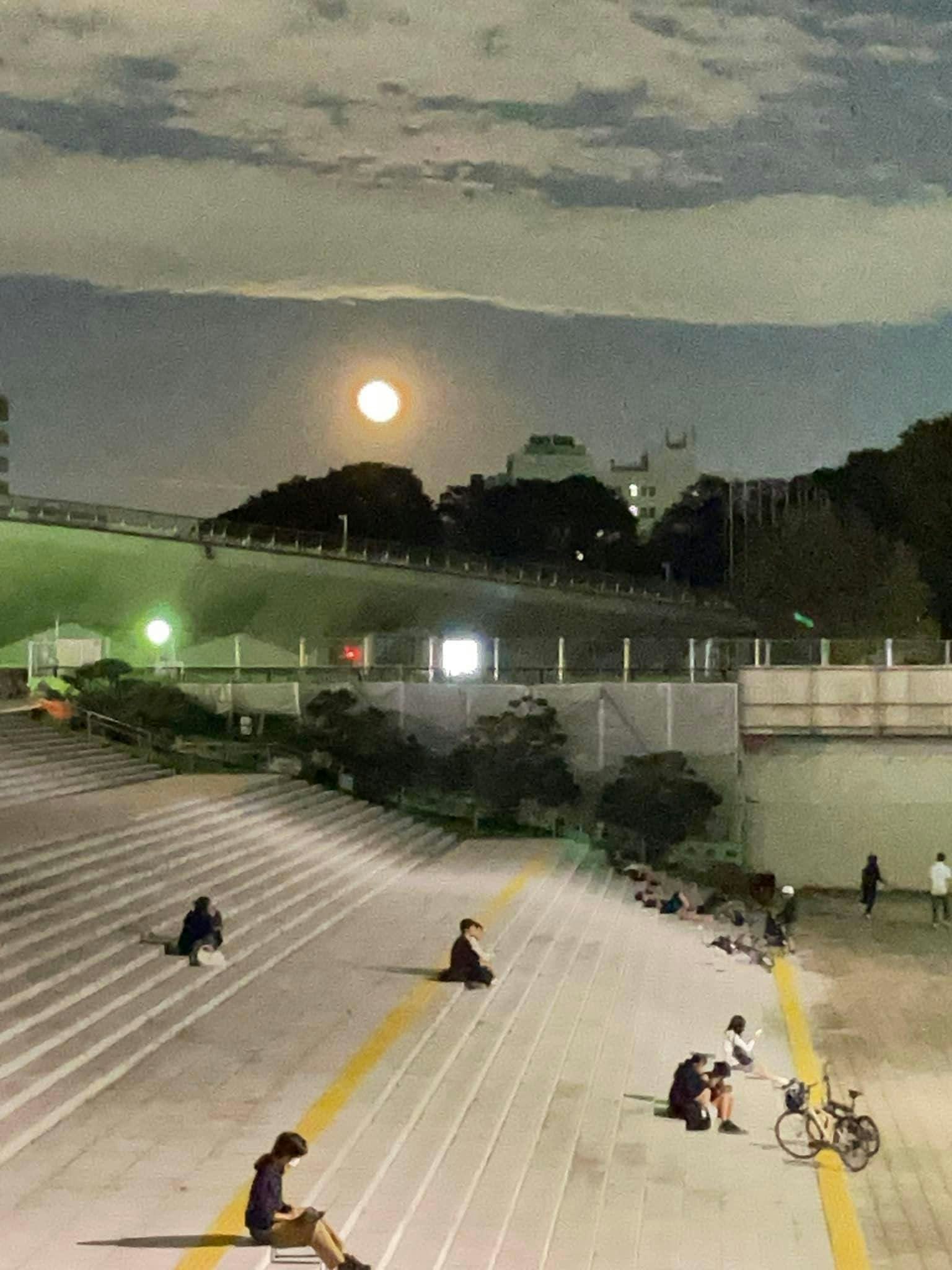 밤하늘에 큰 달과 계단에 앉아 있는 사람들