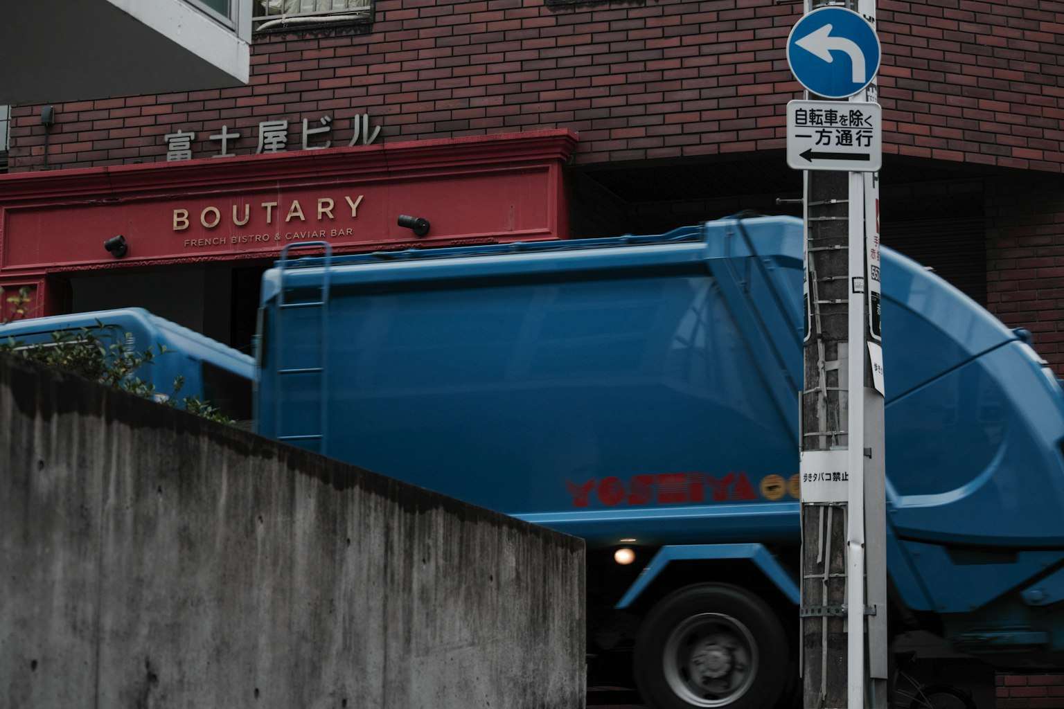 Un camión de basura azul pasando frente a un letrero de Boutary
