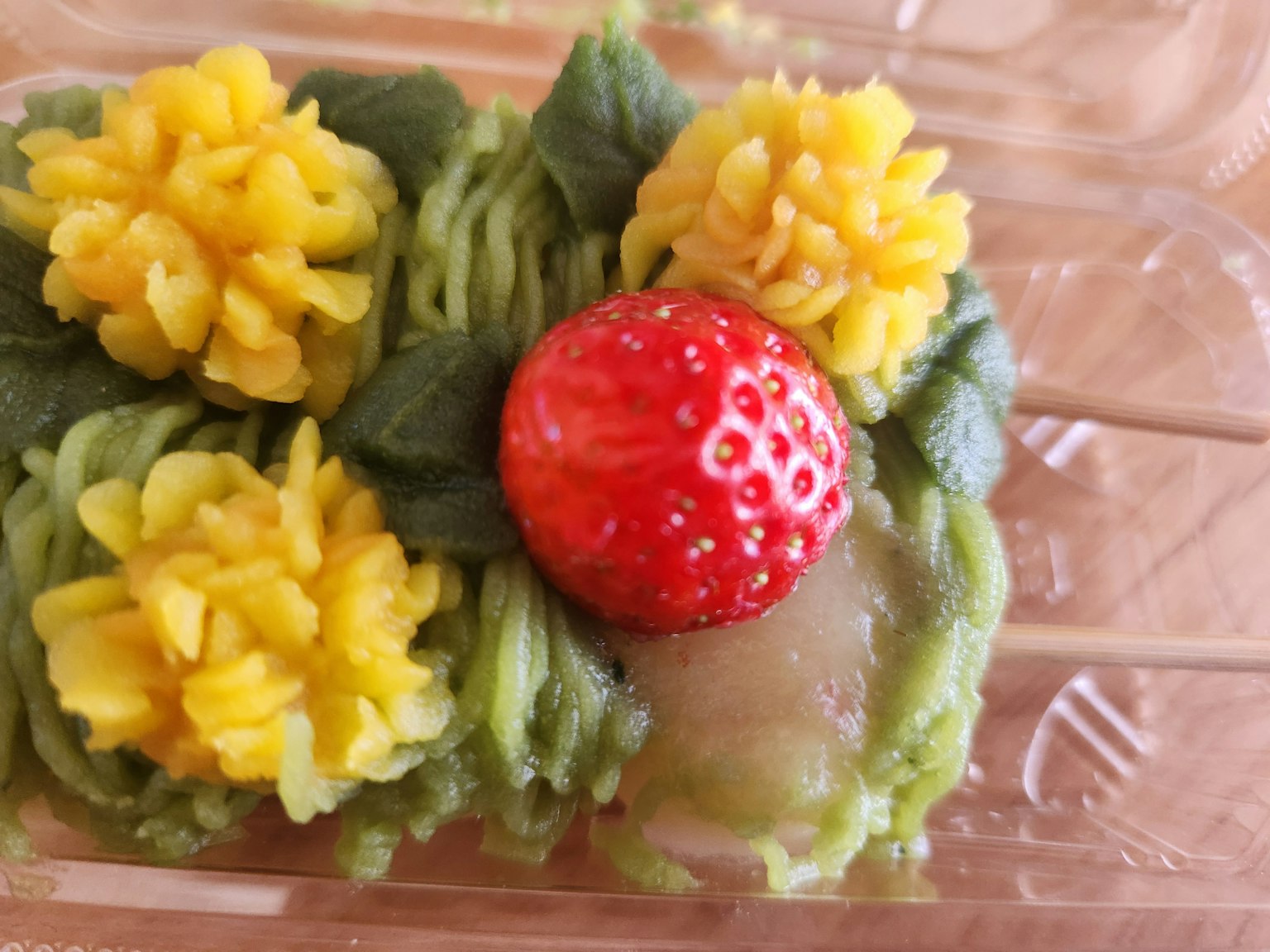 ขนมสีเขียวประดับด้วยดอกไม้สีเหลืองและสตรอเบอรีสีแดง