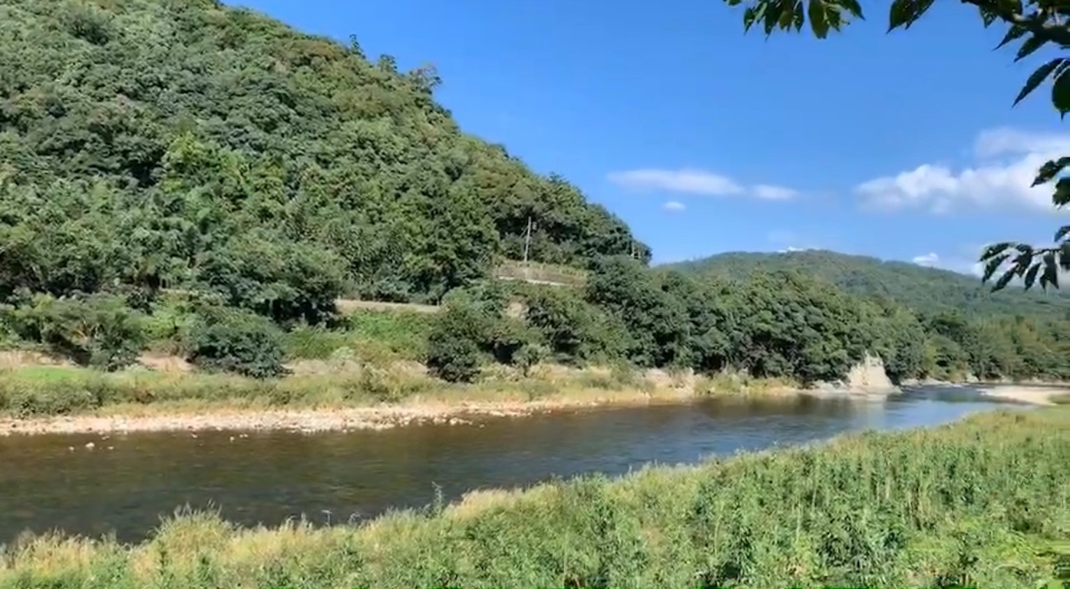 宁静的河流风景，绿丘在晴朗的蓝天下