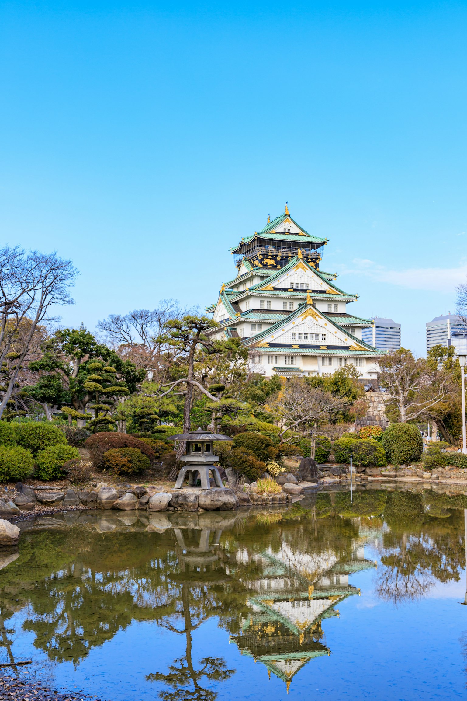 大阪城在池塘中倒影的美丽景观，周围环绕着花园