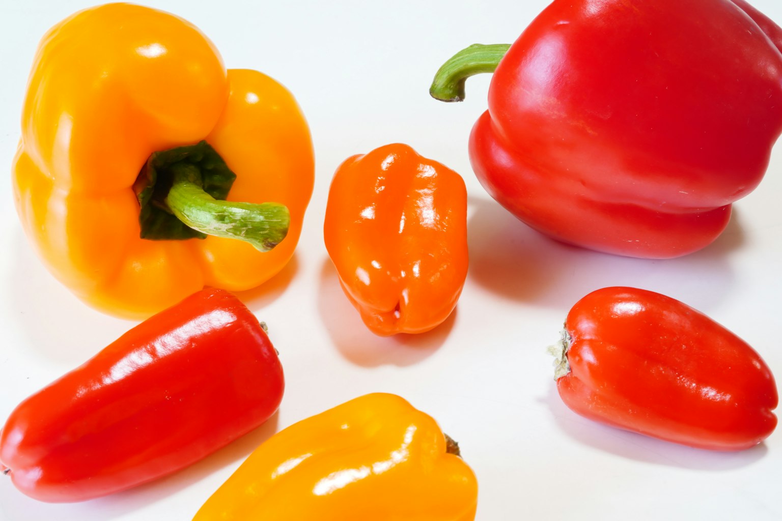 Poivrons colorés et petits piments disposés sur une surface blanche