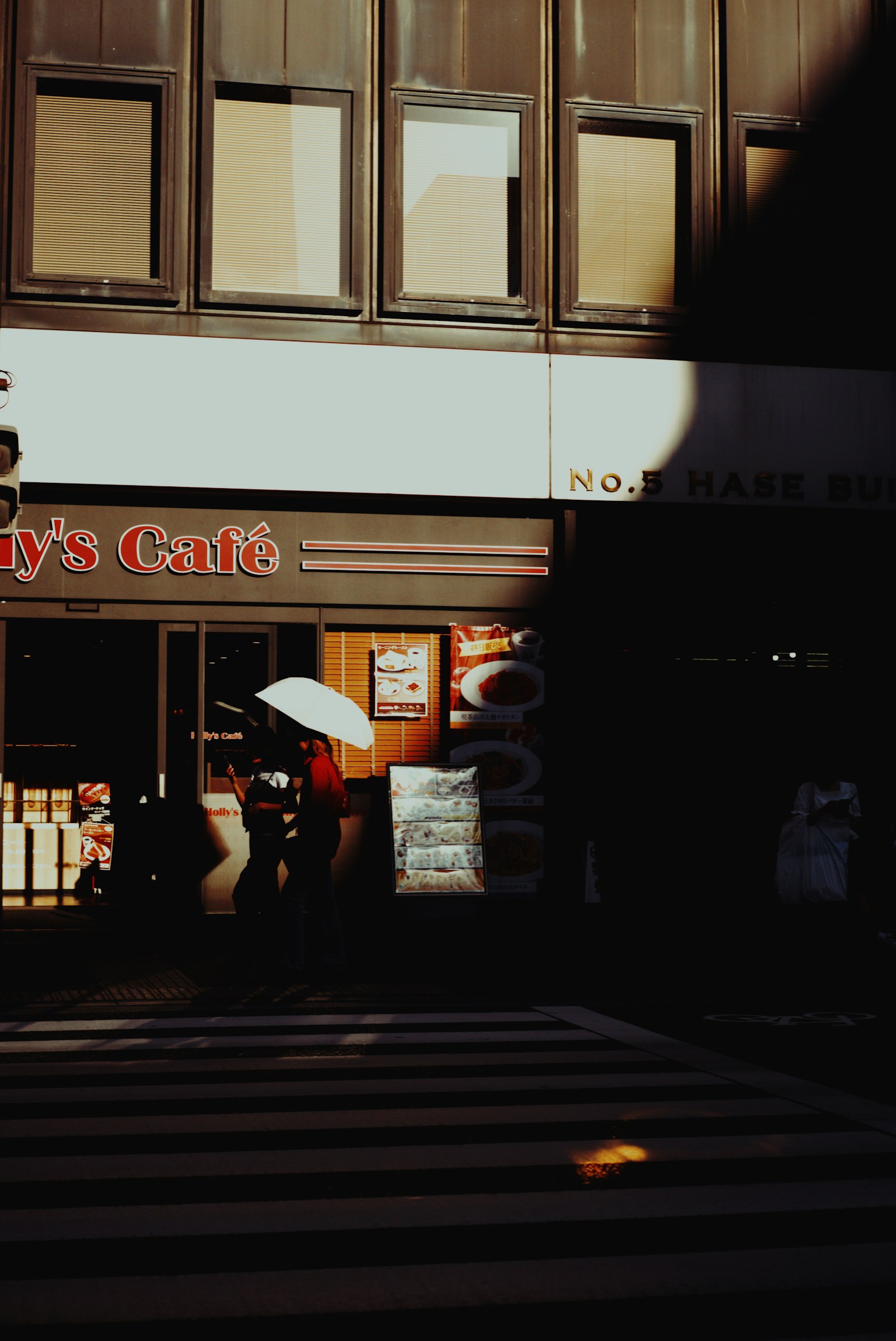 Street view featuring a café with a person holding an umbrella