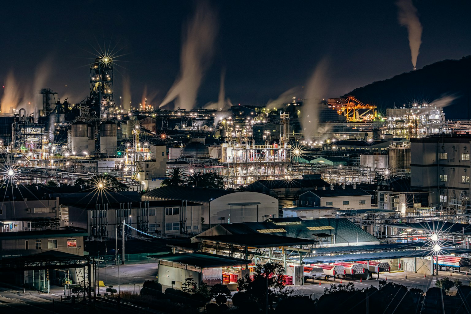 Night industrial landscape with bright lights and smoke from chimneys
