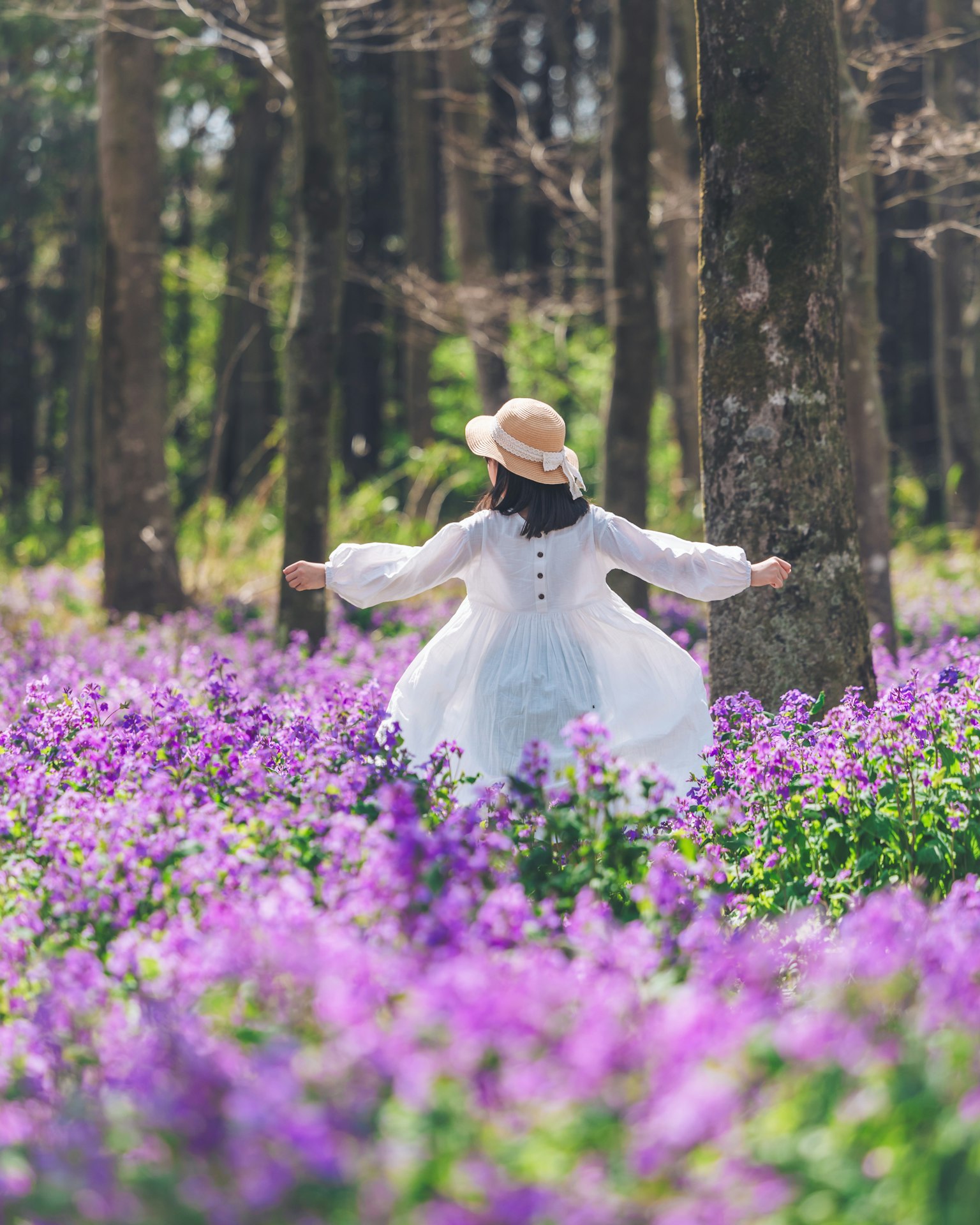 Femme en robe blanche dansant joyeusement parmi des fleurs violettes