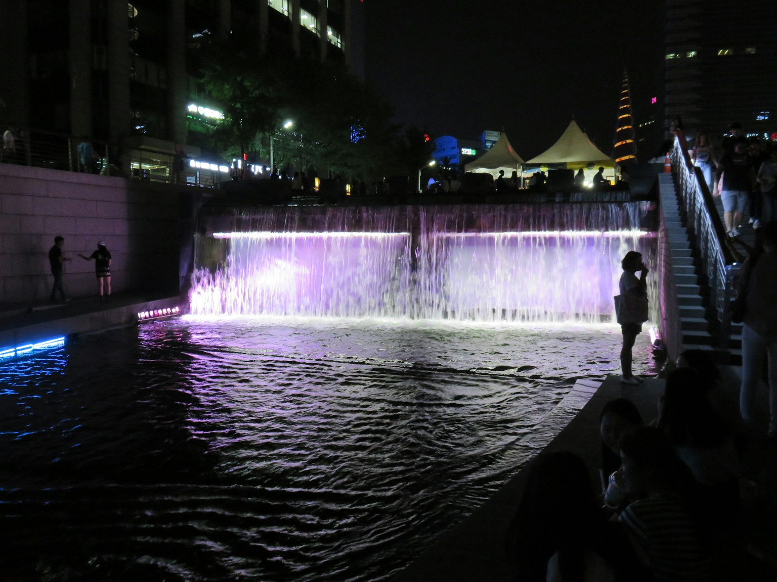 Artificial waterfall at night with colorful lighting and a serene water surface