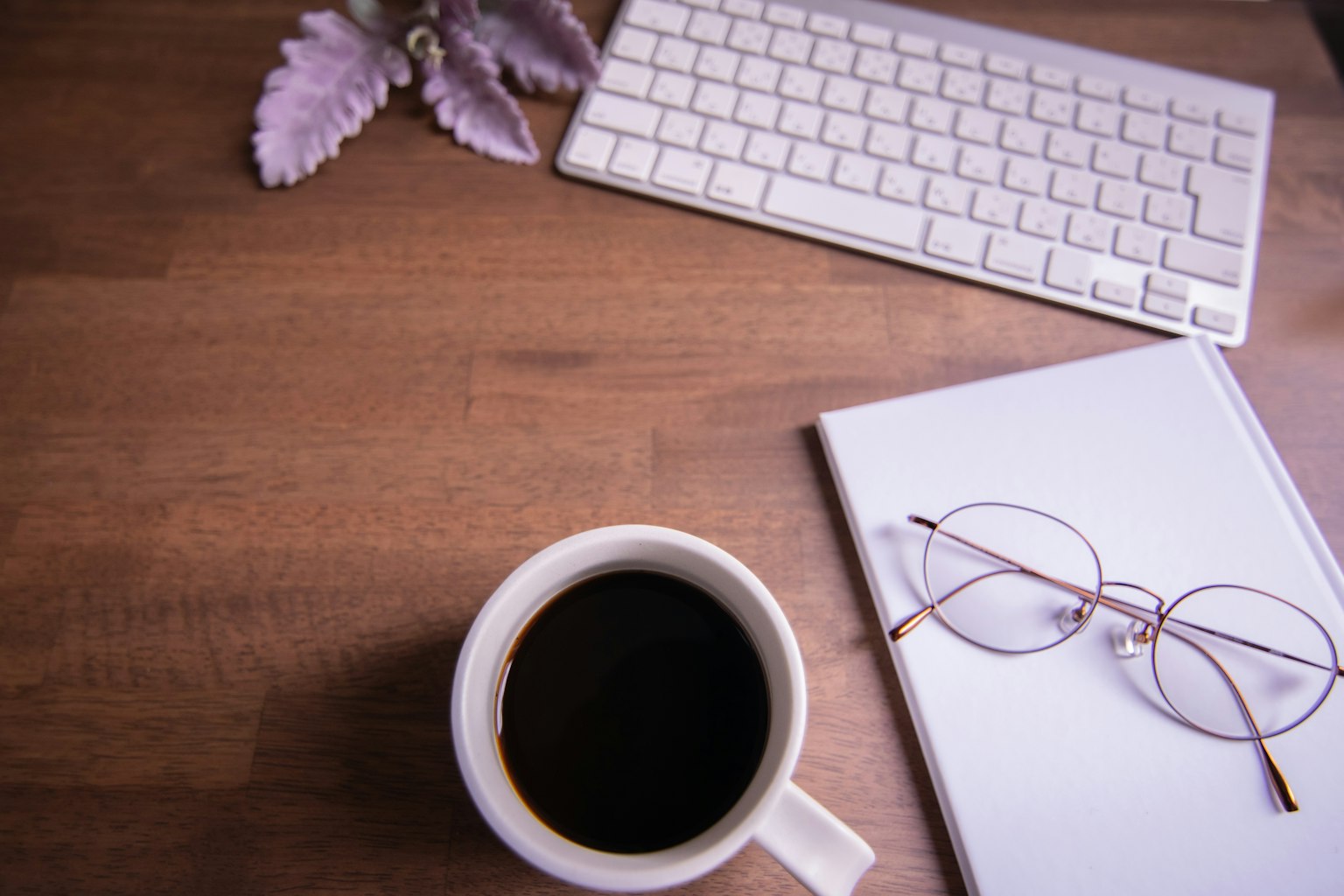나무 책상 위에 커피 컵, 안경, 노트북이 놓여 있다
