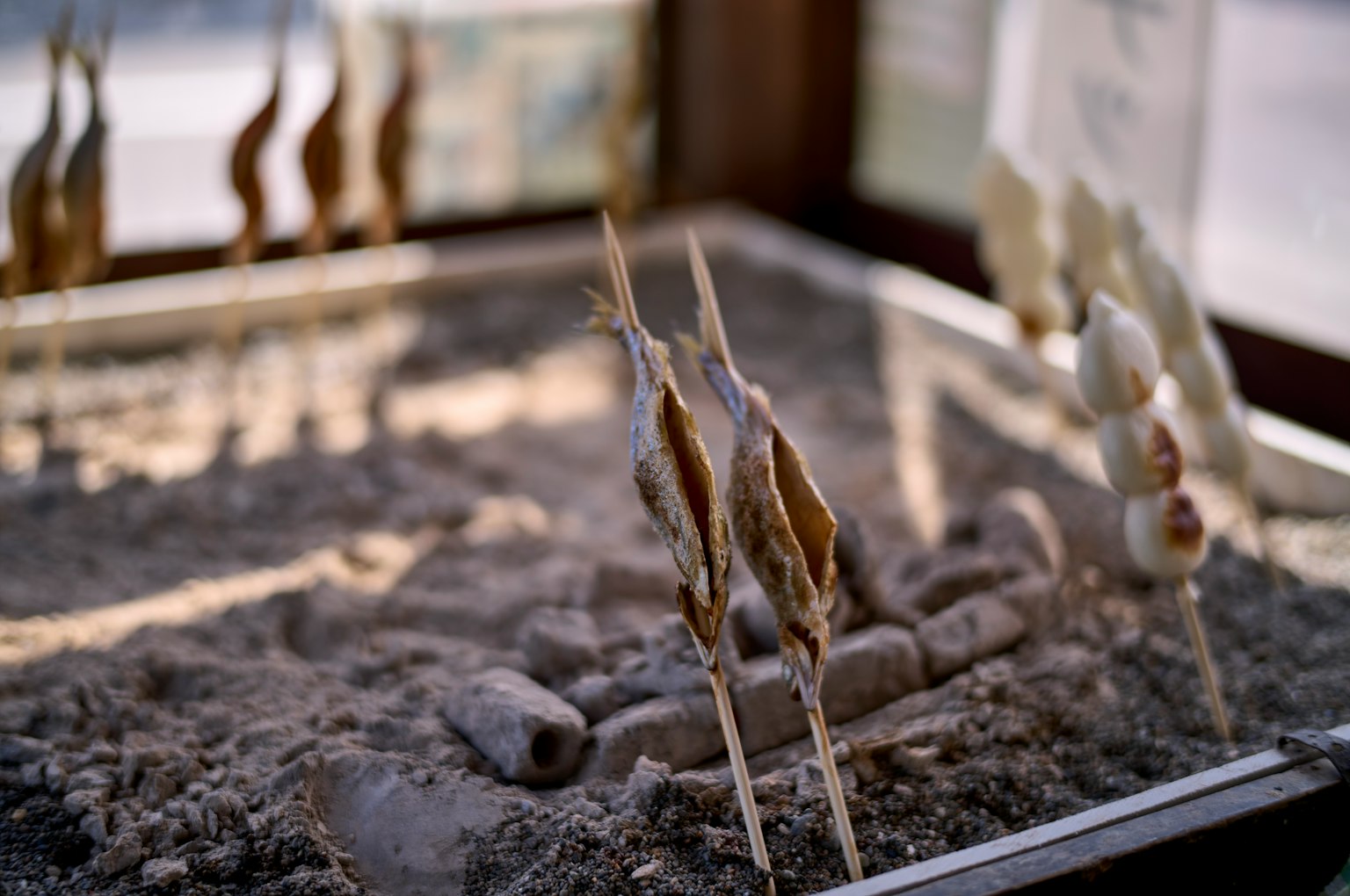 Sticks with grilled items and white spheres in a sand tray