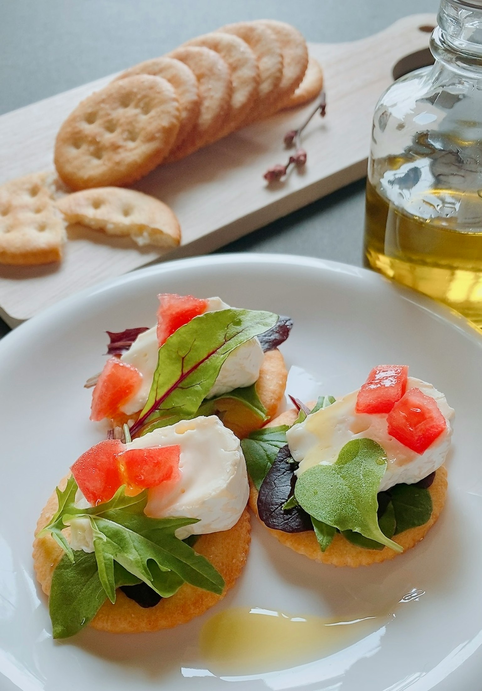 Appetizer with salad and tomatoes on a white plate olive oil bottle and crackers in the background