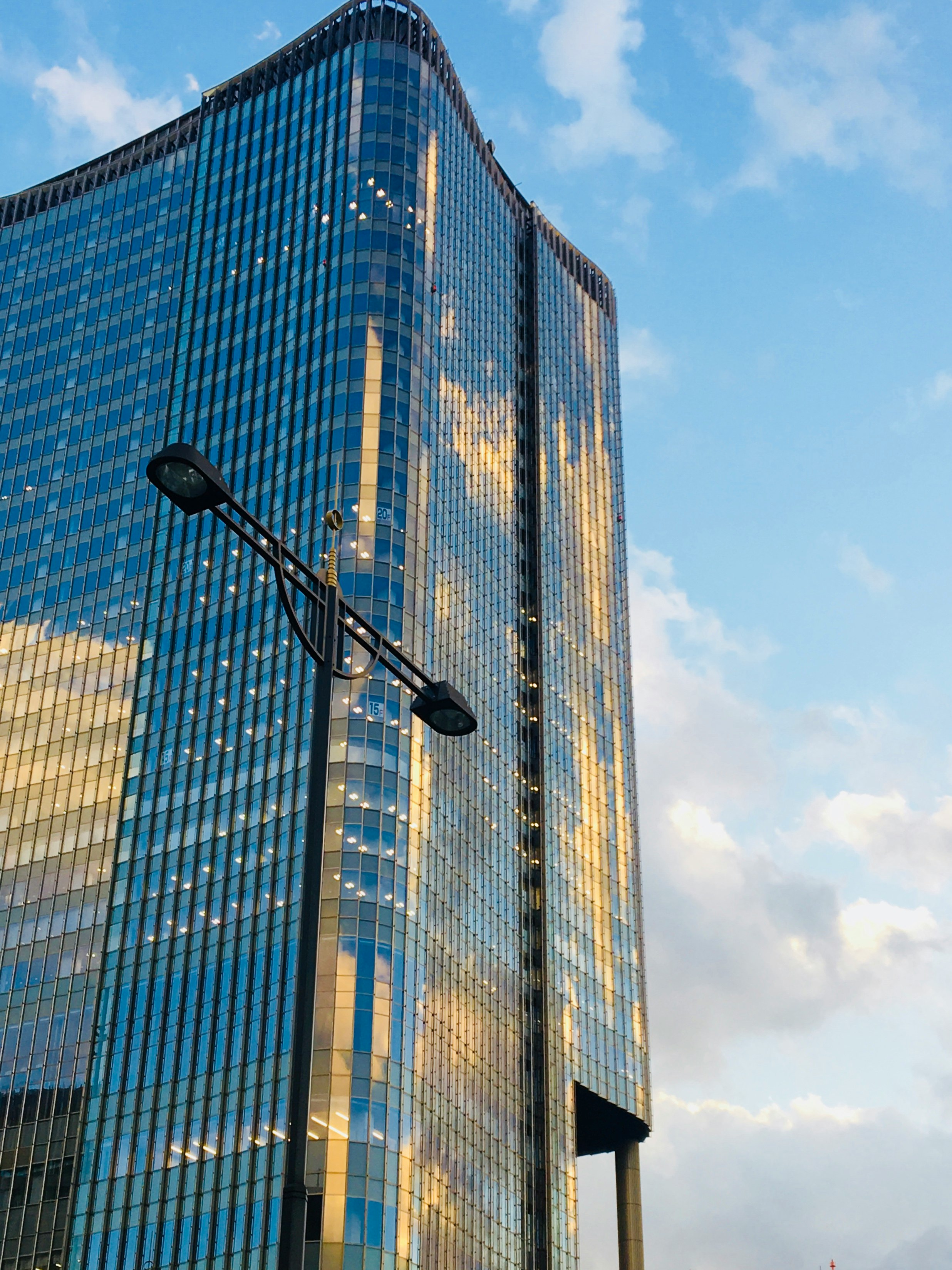 Glas-Hochhaus und Straßenlaternen unter blauem Himmel