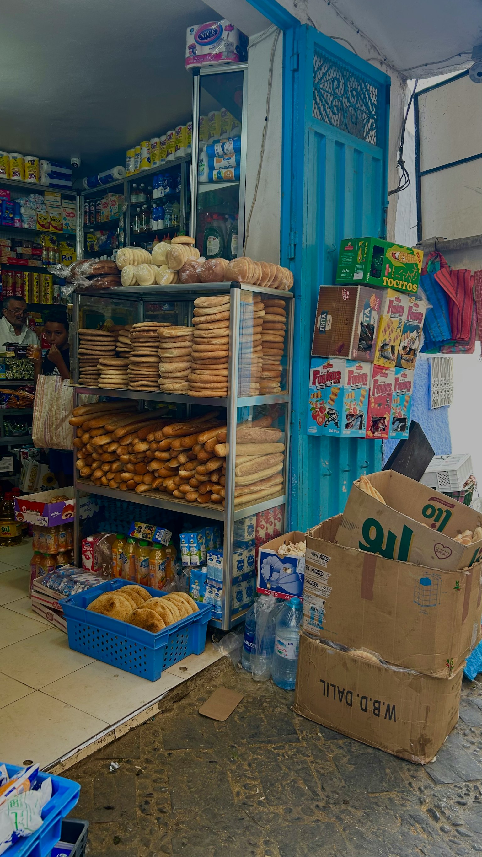 Interior toko kecil dengan rak berisi roti dan bahan makanan di dinding biru