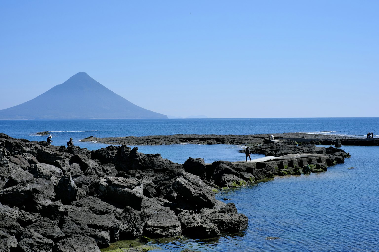 Scenic view of a volcano and ocean under a clear blue sky with rocky shoreline