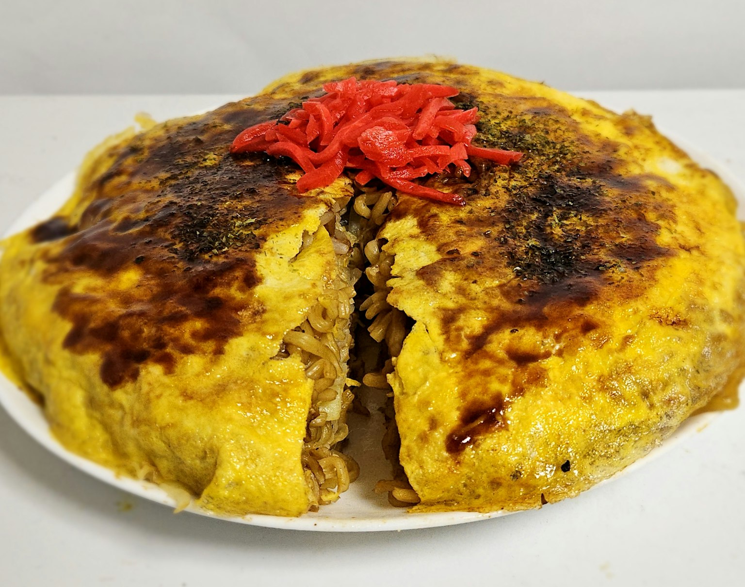 Ein Gericht, das okonomiyaki ähnelt, mit Ei belegt und mit eingelegtem Ingwer garniert