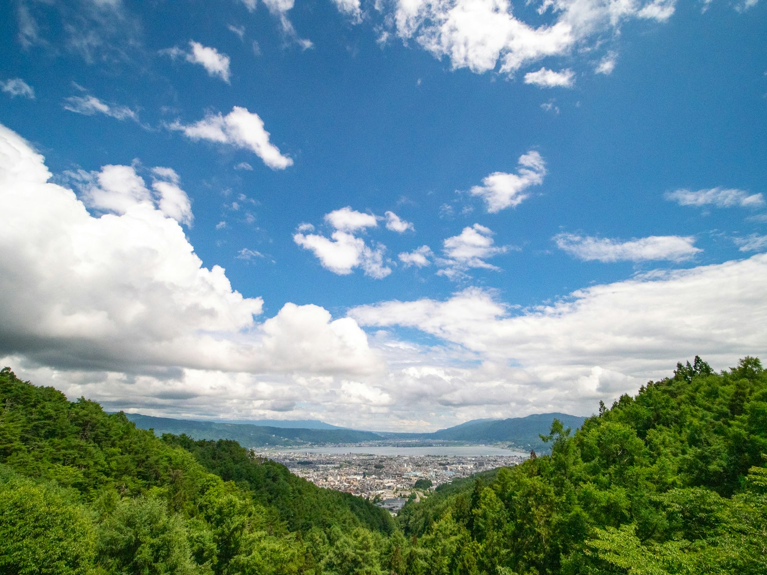 Scenic view of a blue sky with white clouds green mountains and a distant city landscape