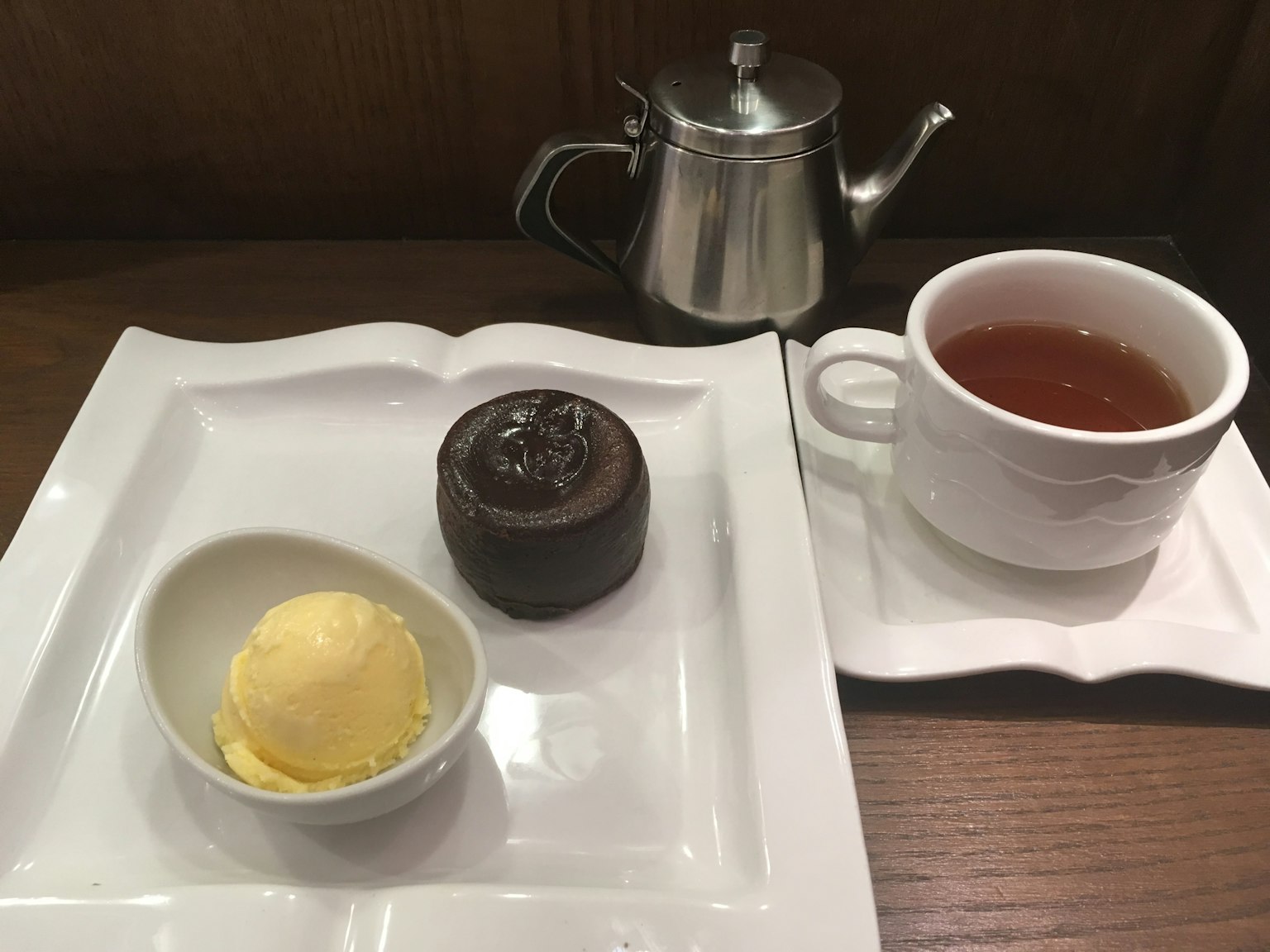 A dessert plate featuring ice cream, chocolate cake, and a teapot with a cup of tea