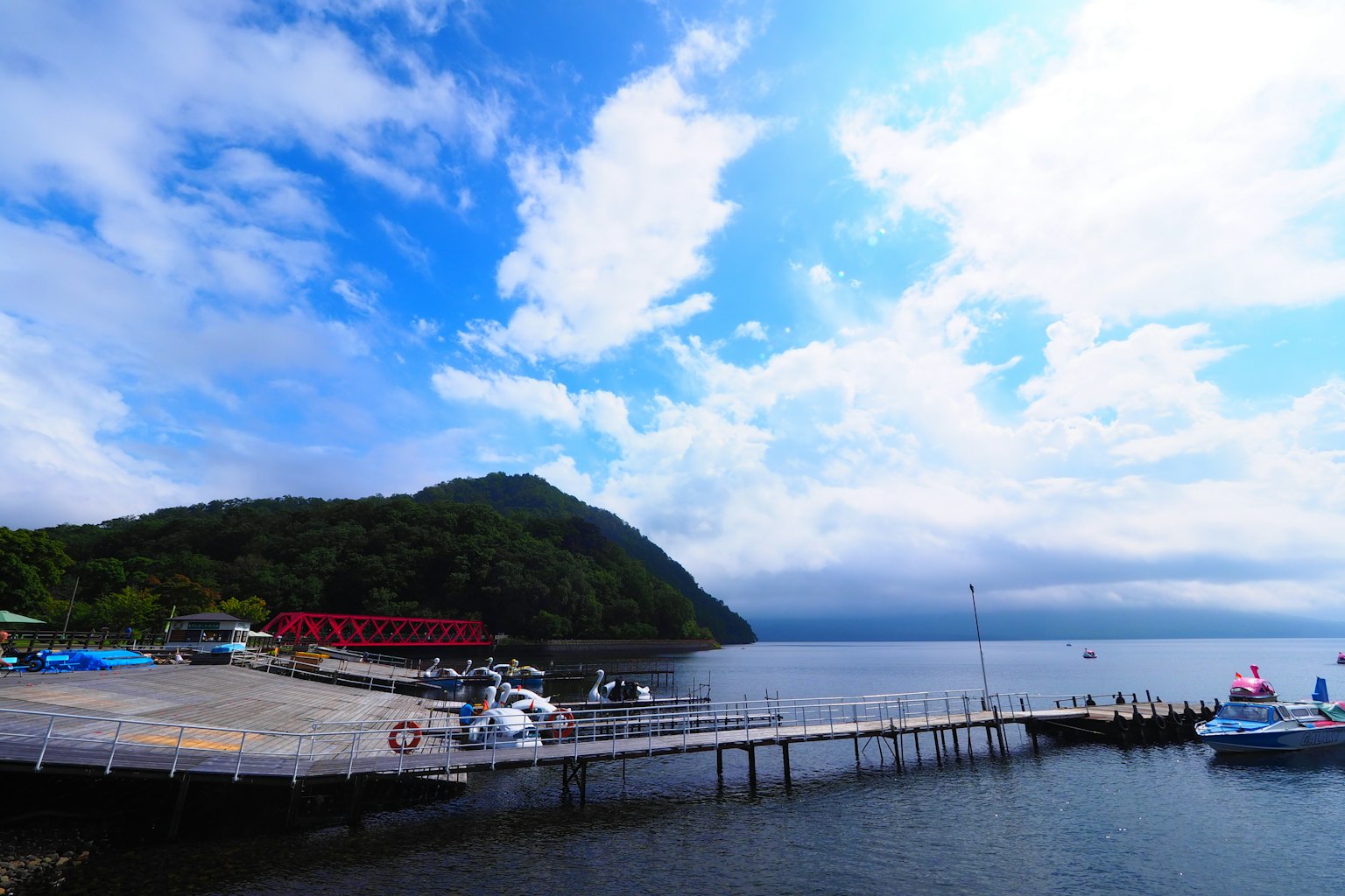 Küstenlandschaft mit blauem Himmel und Wolken Boote am Pier und grüne Hügel