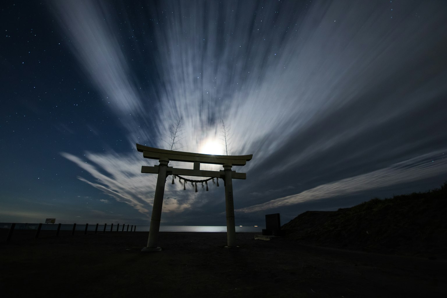 Torii gate illuminated by moonlight with dramatic clouds in the night sky