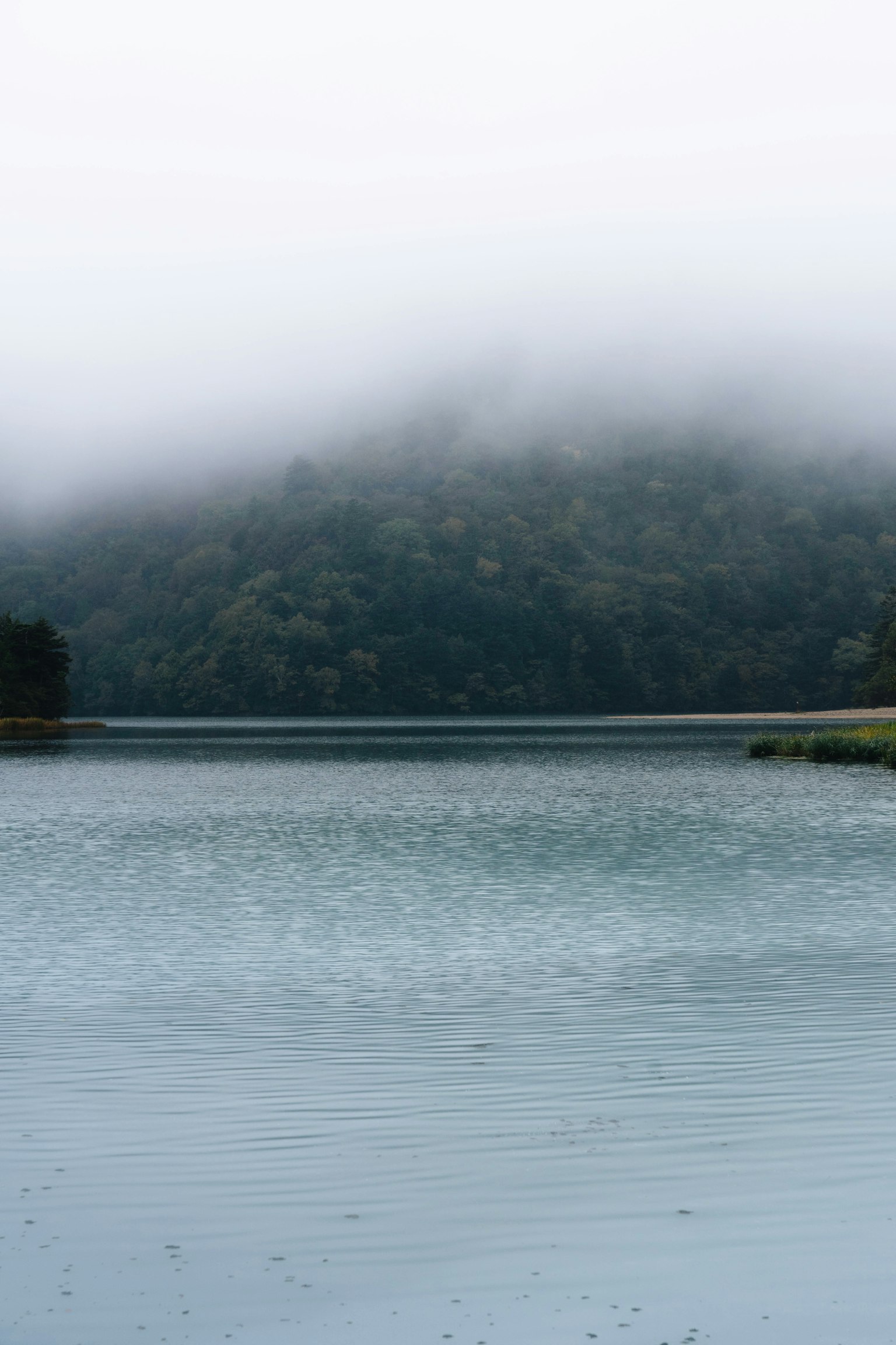 Lago cubierto de niebla con una montaña a lo lejos