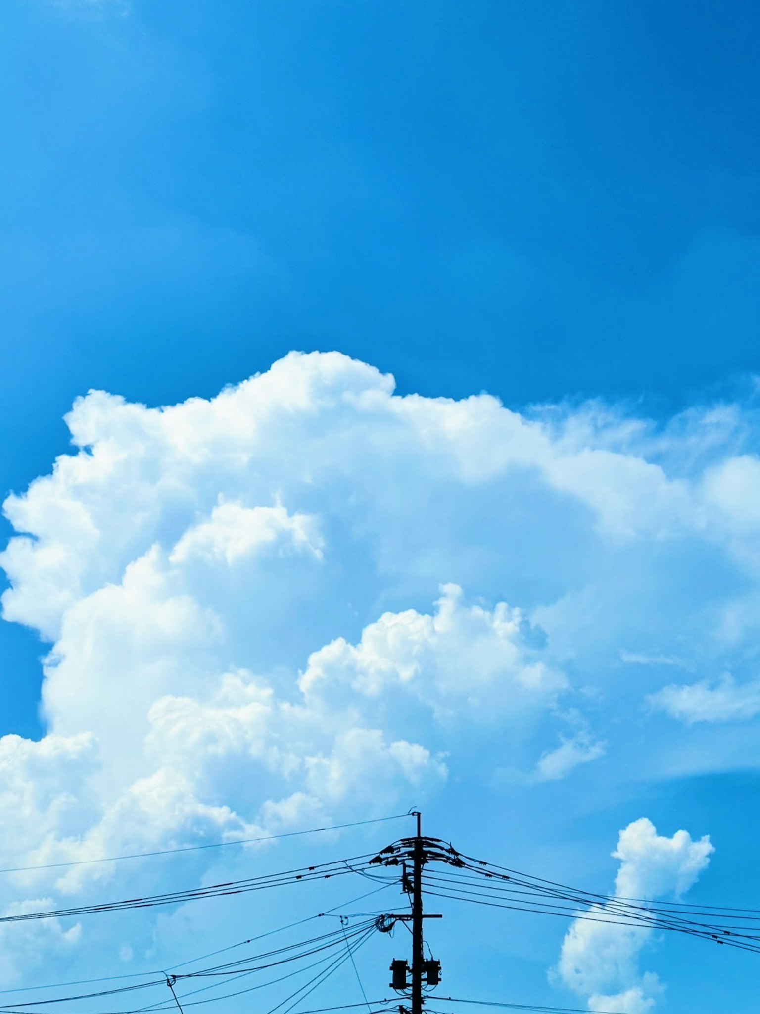 Bright blue sky with fluffy white clouds visible electric wires at the bottom