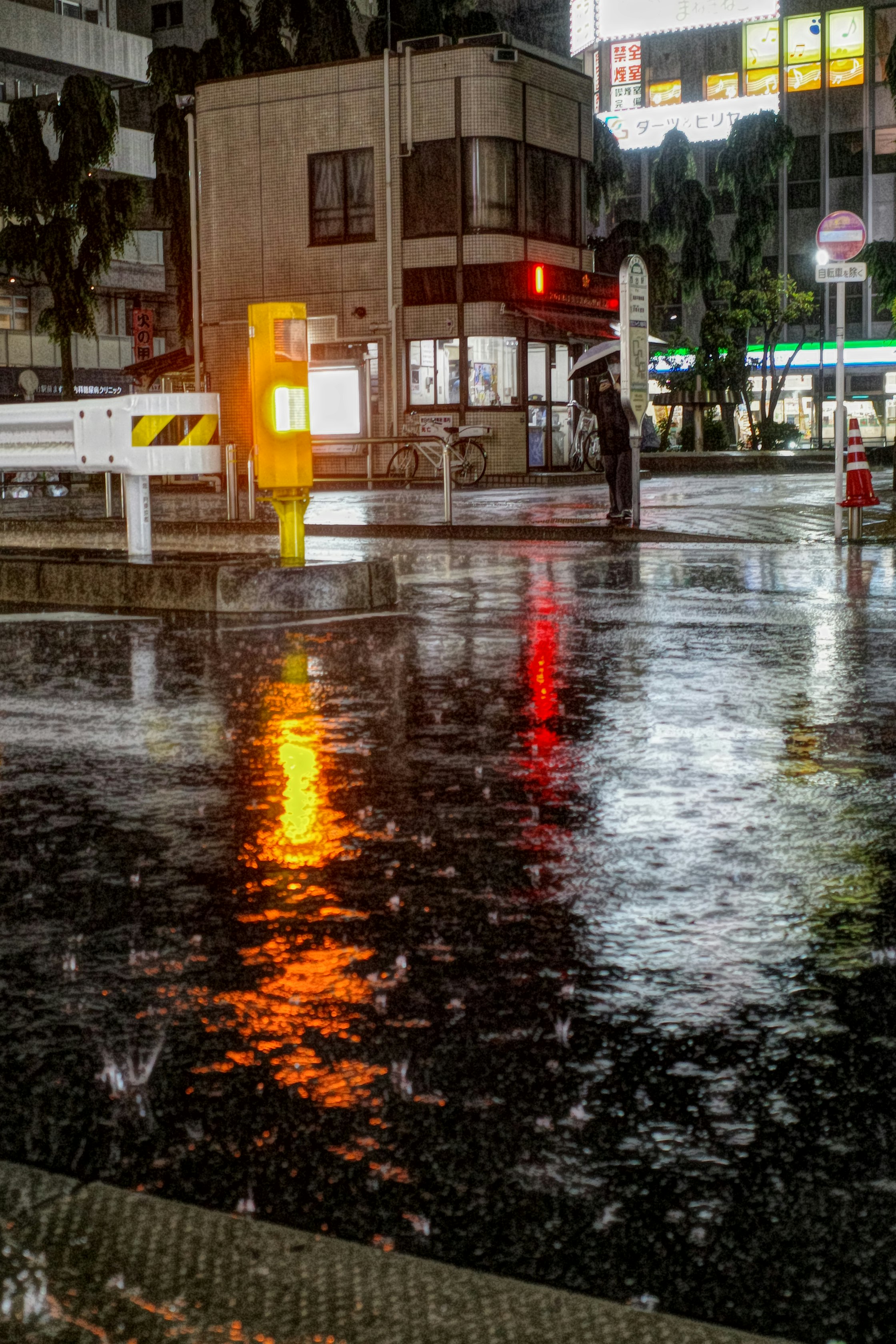 Straßenecke nach dem Regen mit leuchtenden Ampeln und Spiegelungen auf nassem Asphalt