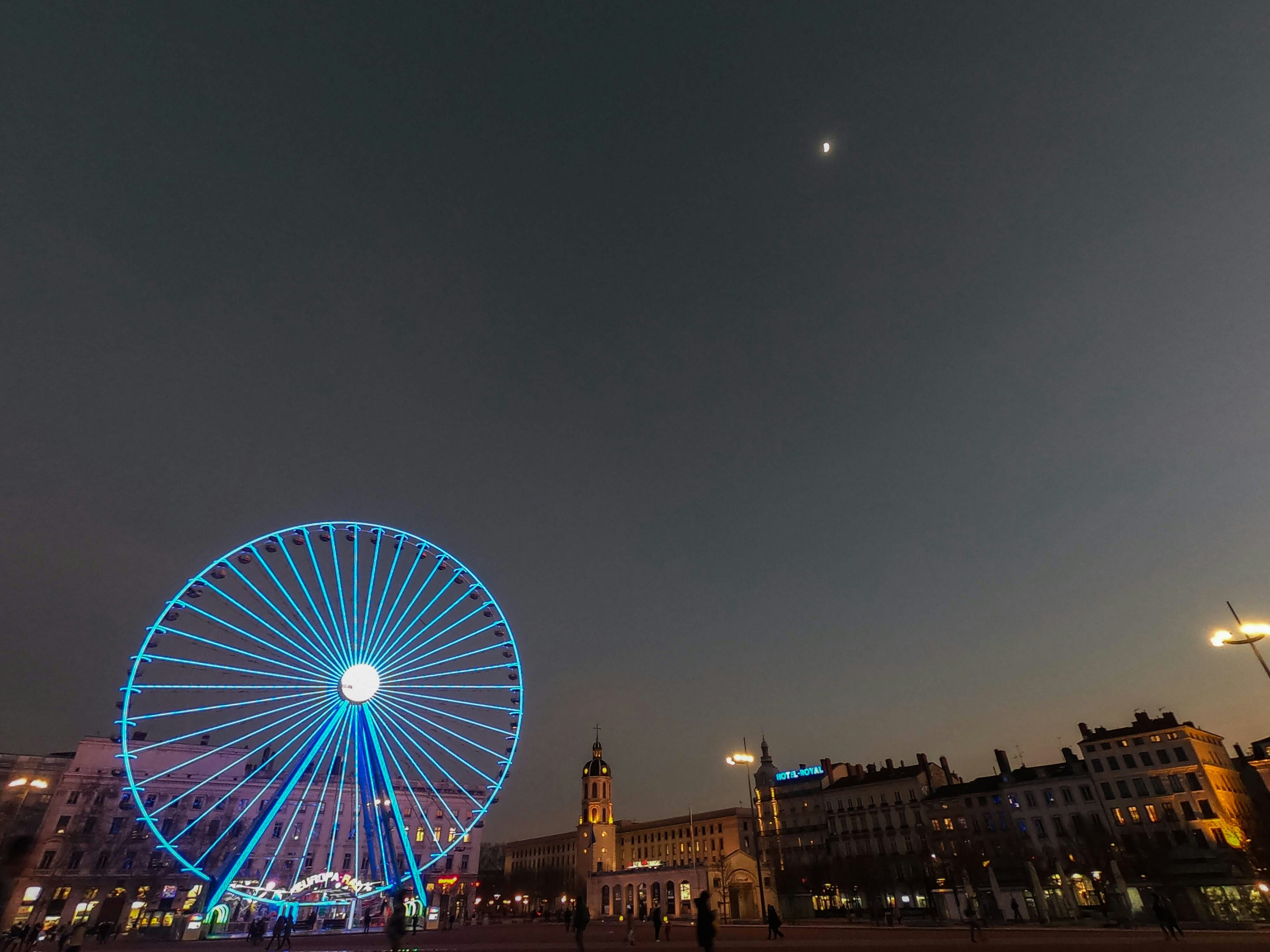 Nachtansicht der Straßen von Lyon mit einem blau beleuchteten Riesenrad auf einem Platz