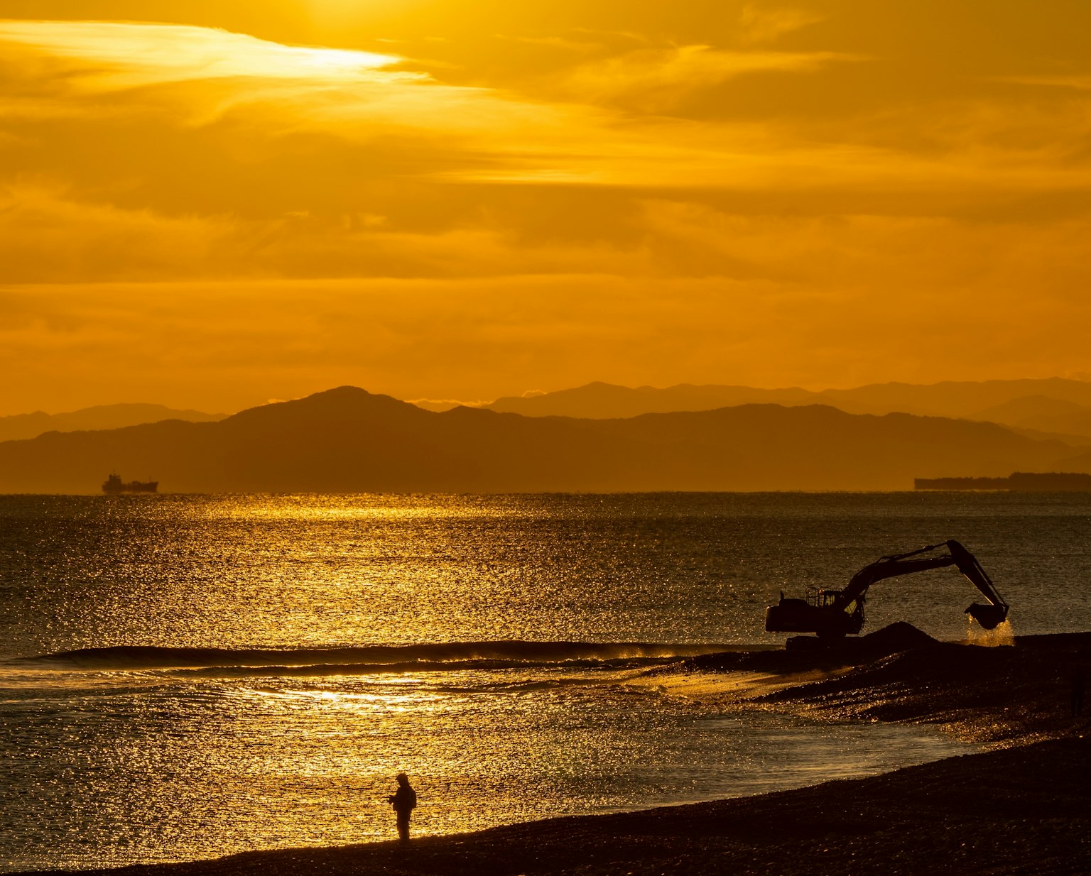Silhouette di una persona su una spiaggia con macchinari al tramonto