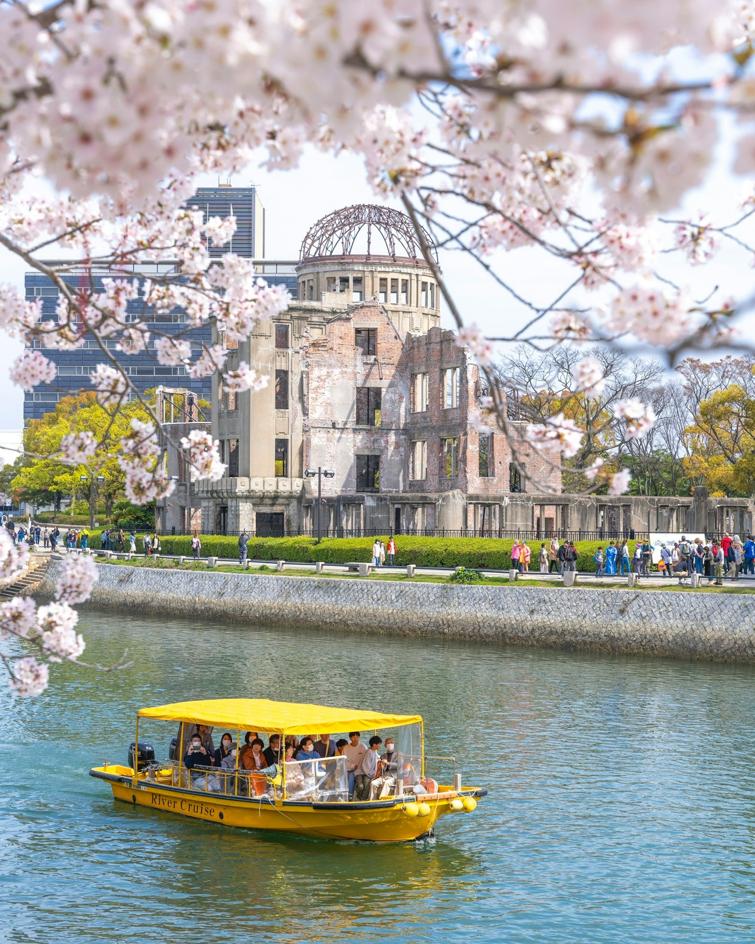 Cảnh quan của Dome Bom Nguyên Tử Hiroshima với hoa anh đào trên sông và một chiếc thuyền màu vàng