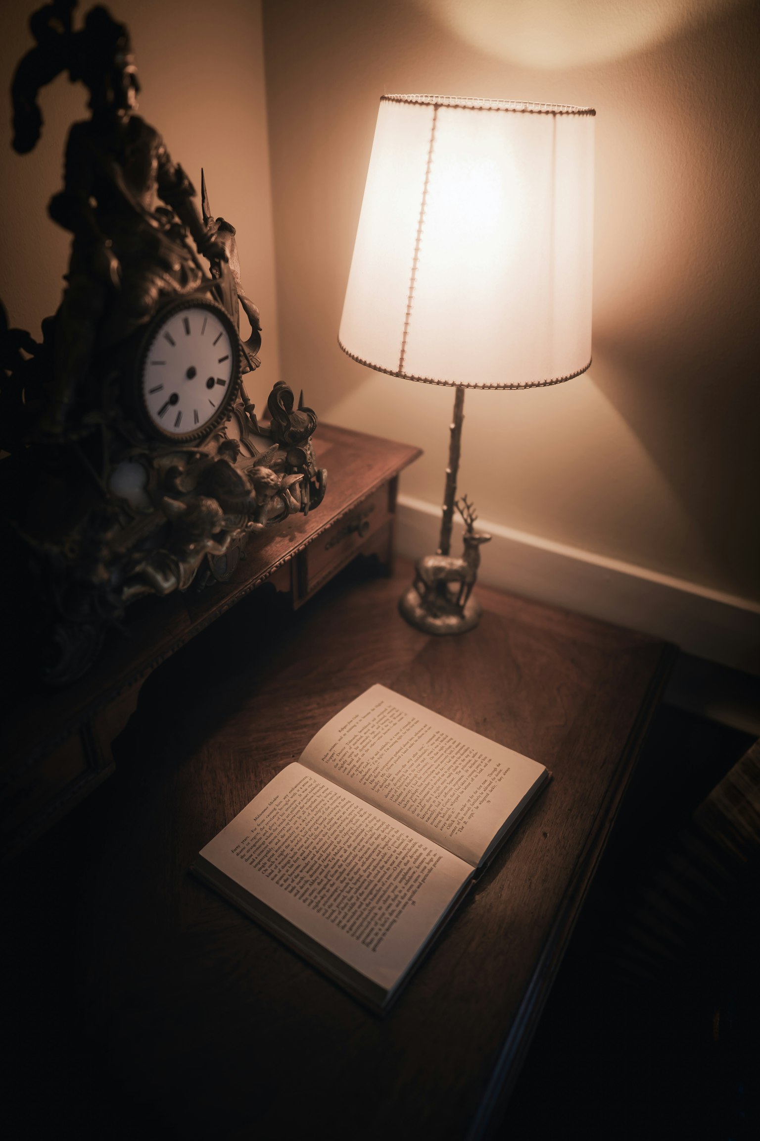 Sebuah buku catatan terbuka di atas meja dengan jam antik dan lampu