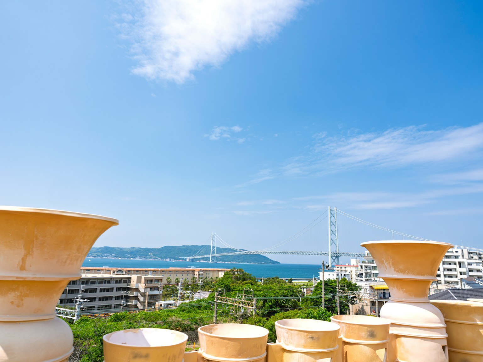 青空の下に並ぶ陶器の鉢と遠くに見える橋の風景