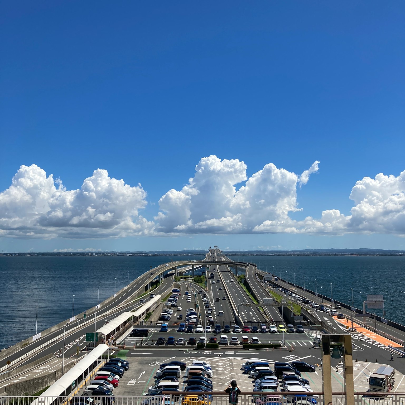 Long bridge extending over the water with a clear blue sky and white clouds
