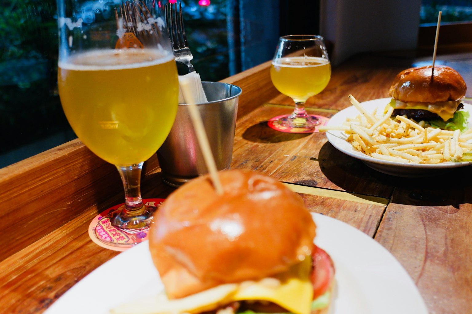 A plate with a burger and fries alongside glasses of beer on a wooden table
