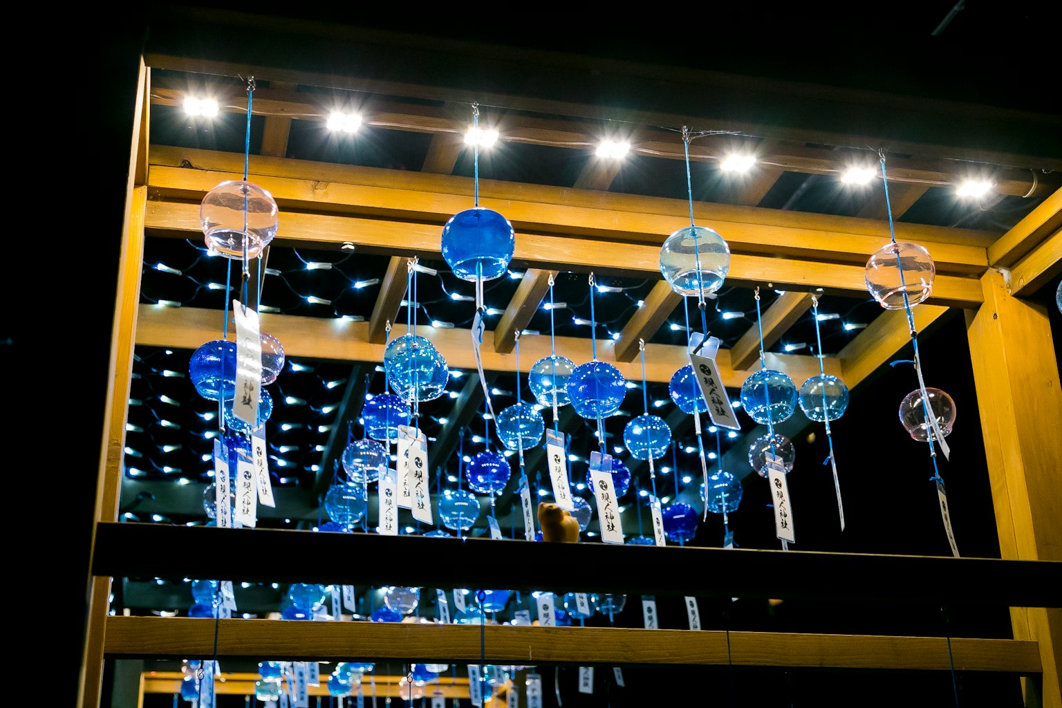 Estructura de madera con campanas de viento azules colgantes iluminadas por luces