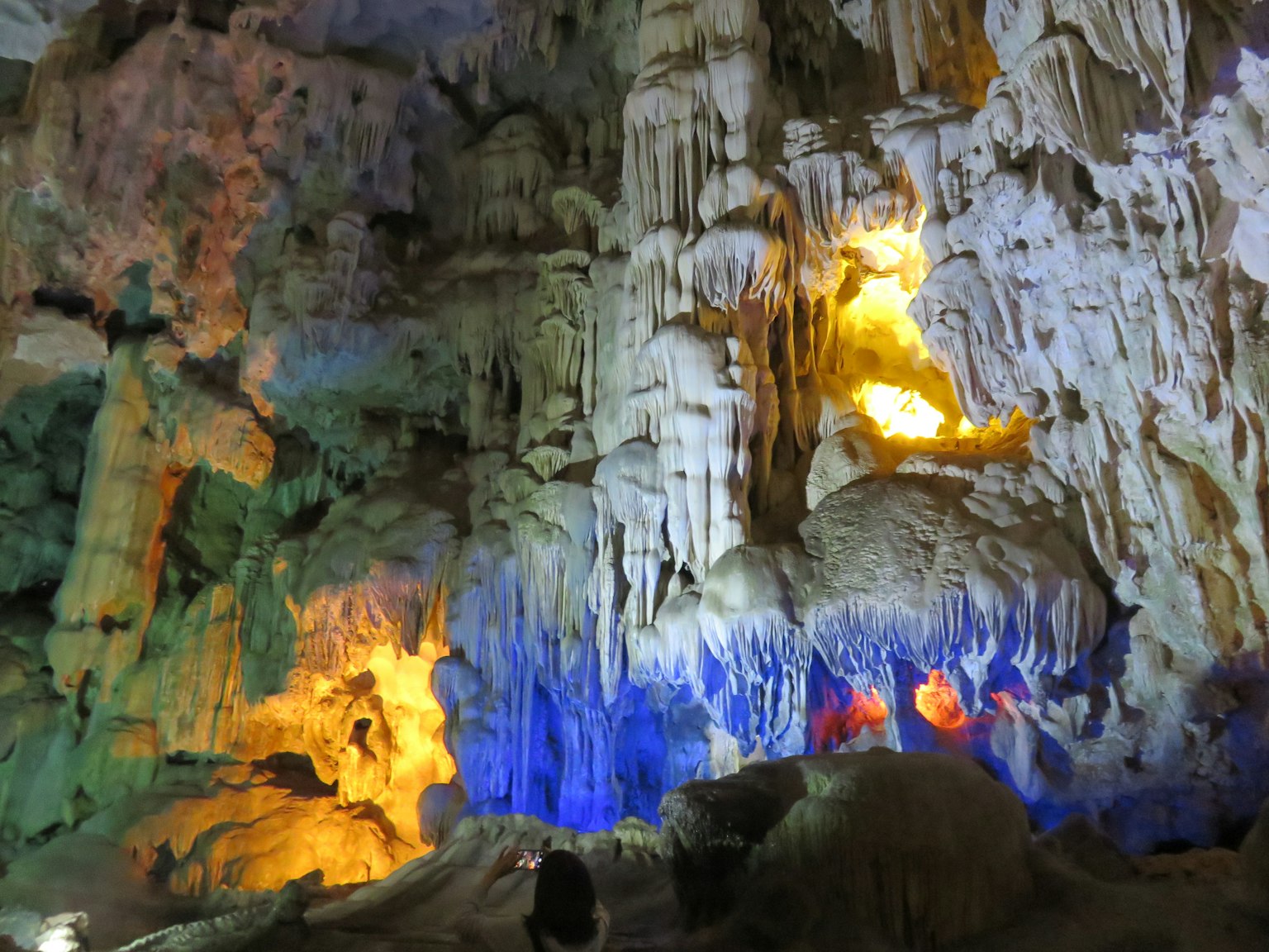 Interior of a cave illuminated by colorful lights highlighting stalactites and stalagmites