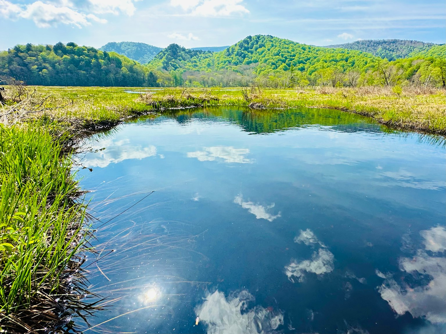 Un estanque sereno que refleja el cielo azul y las nubes rodeado de colinas verdes
