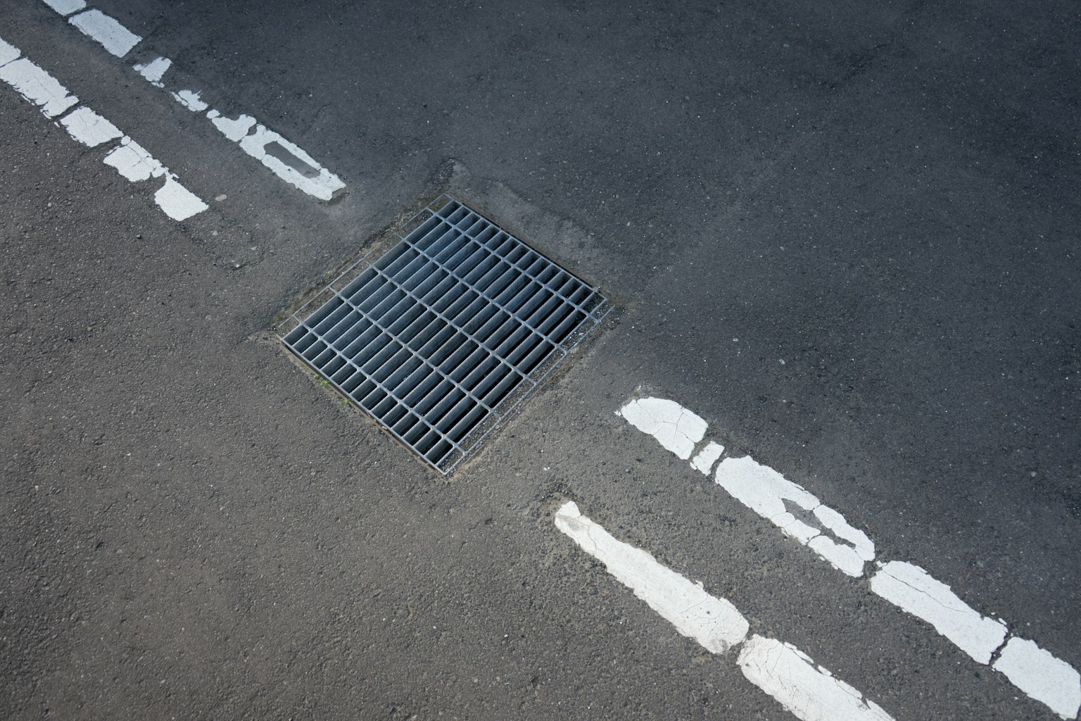 Nahaufnahme eines Metallgitters auf Asphalt mit weißen Linien