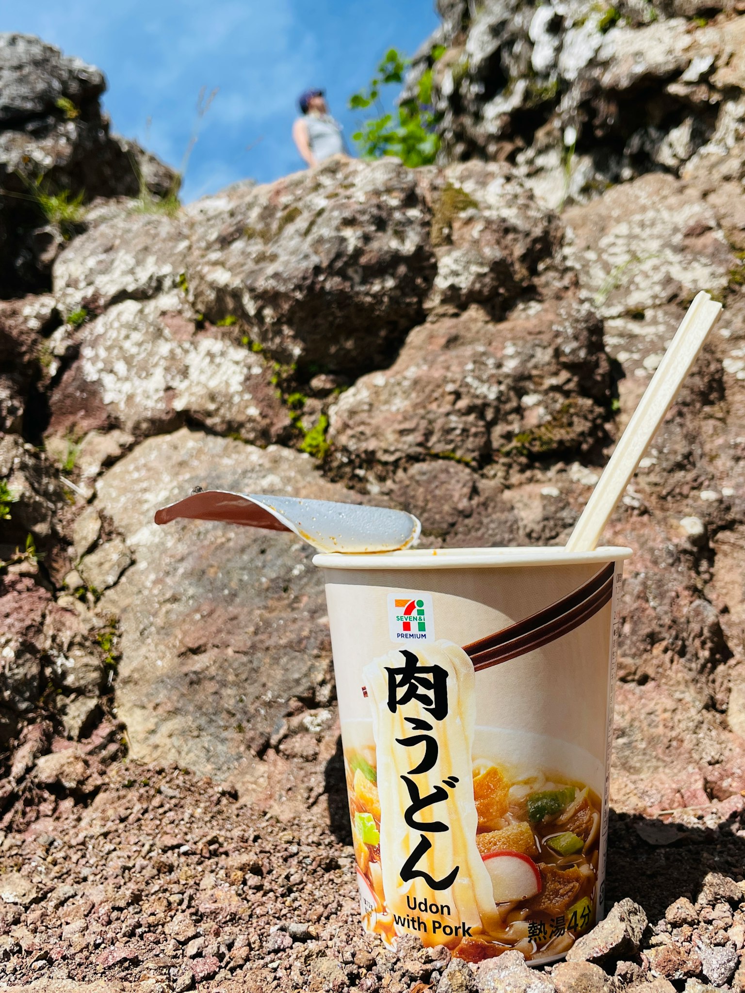 Tasse mit Fleisch-Udon und Löffel auf felsigem Boden