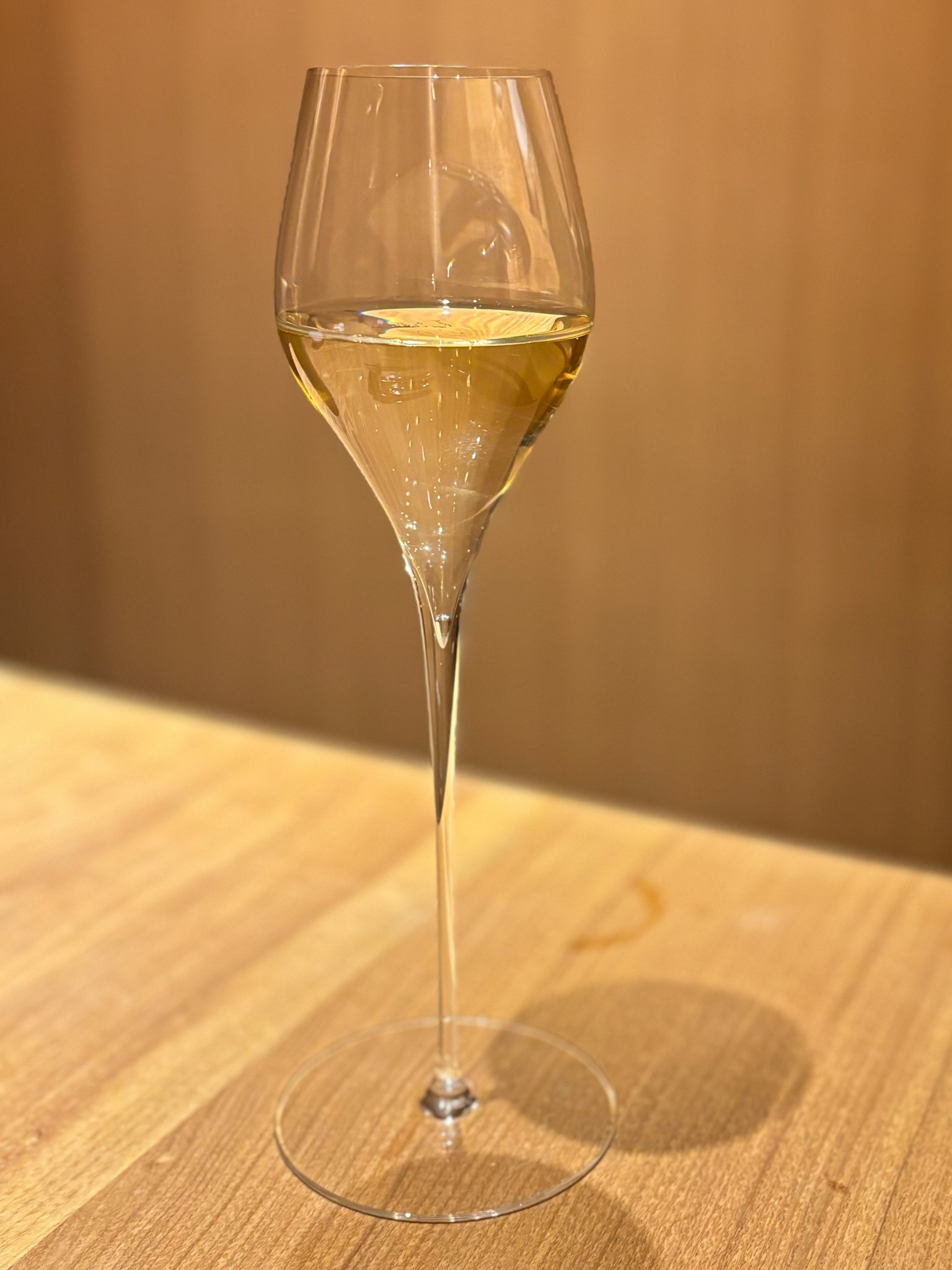 A clear wine glass filled with white wine on a wooden table