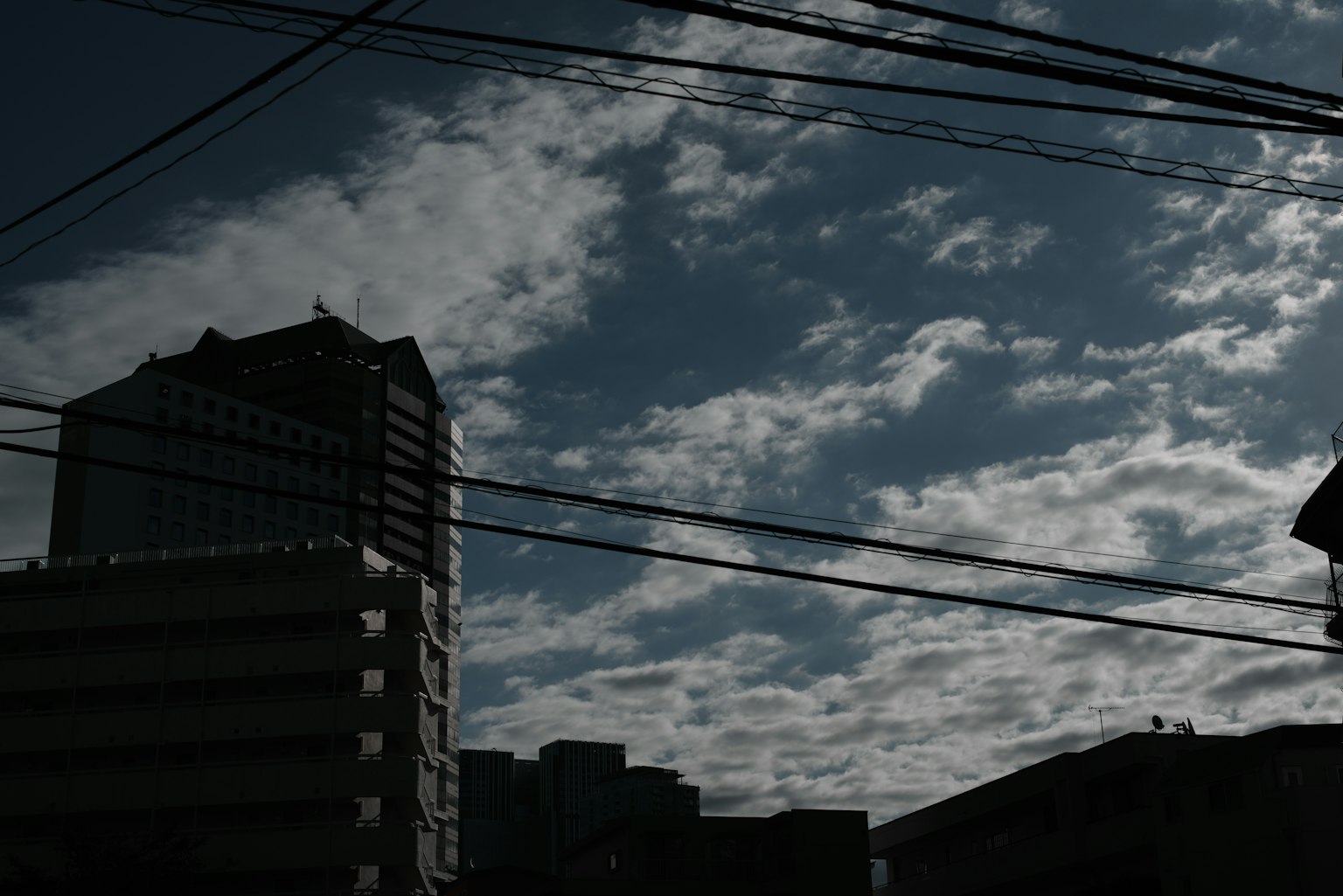 Silhouette de bâtiments contre un ciel nuageux avec des lignes électriques croisées