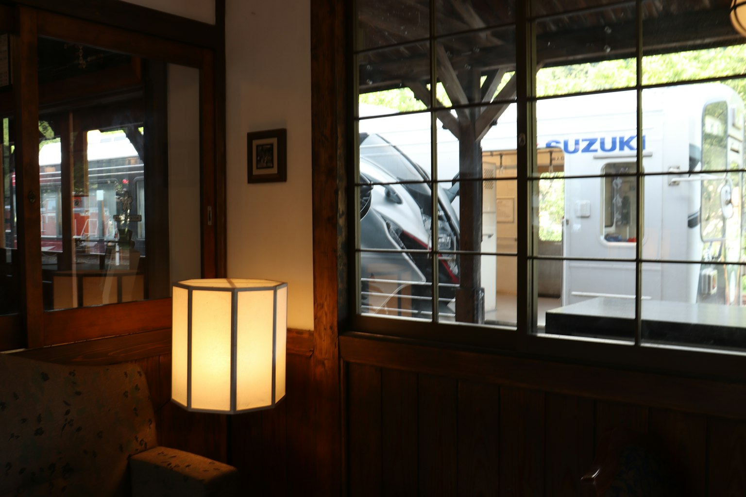 Interior view showing wooden decor and a lamp with a Suzuki trailer visible outside the window