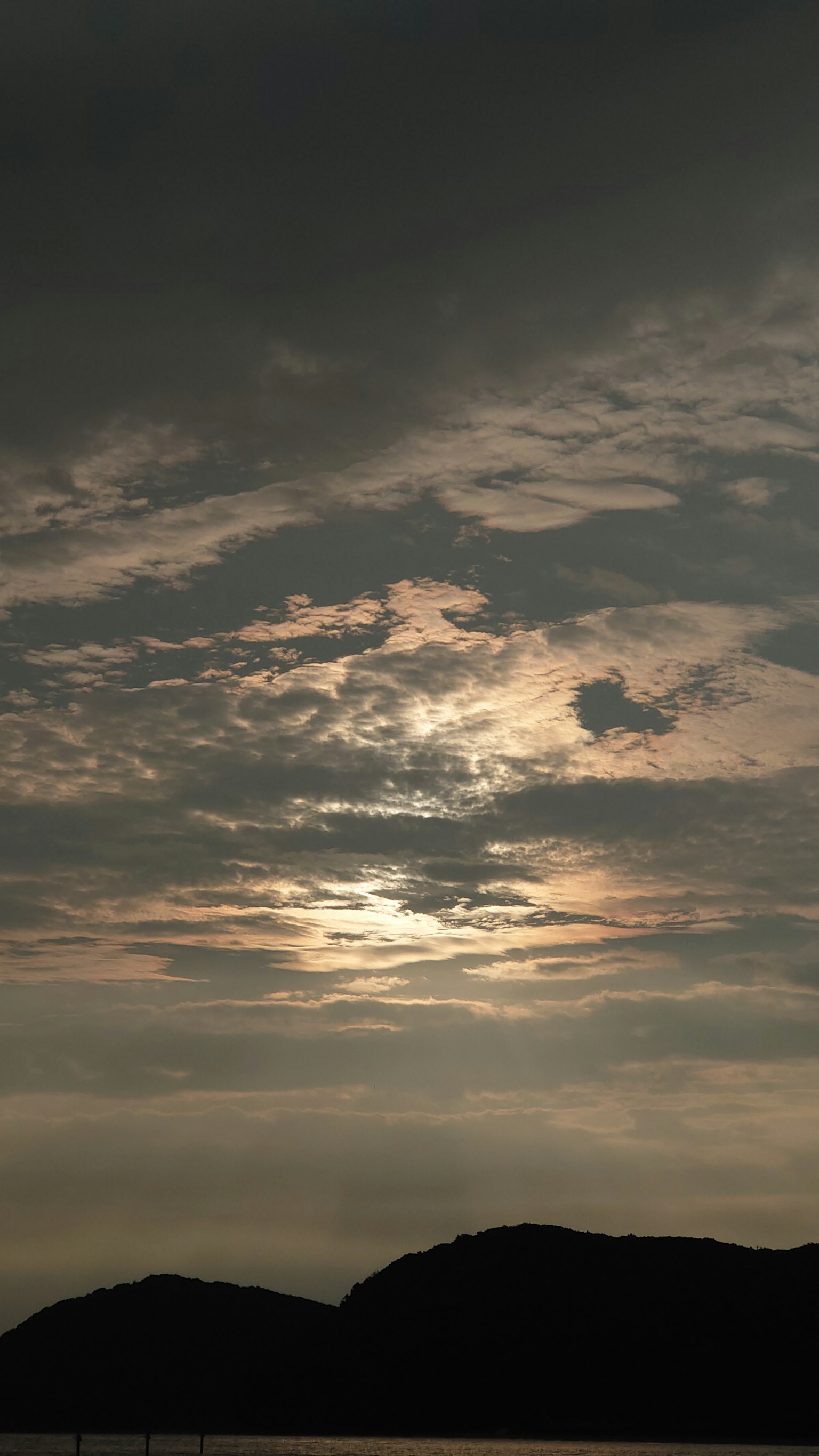 Langit senja yang mendung dengan siluet gunung di latar belakang