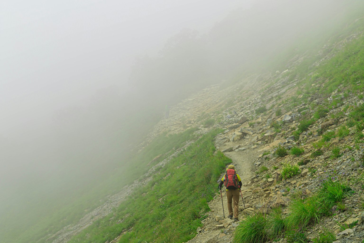 一个在雾中行走的徒步旅行者，周围是岩石小路和绿色草地