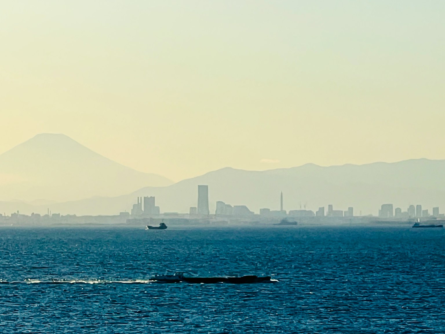 一艘船漂浮在海面上，遠處是山脈和城市天際線